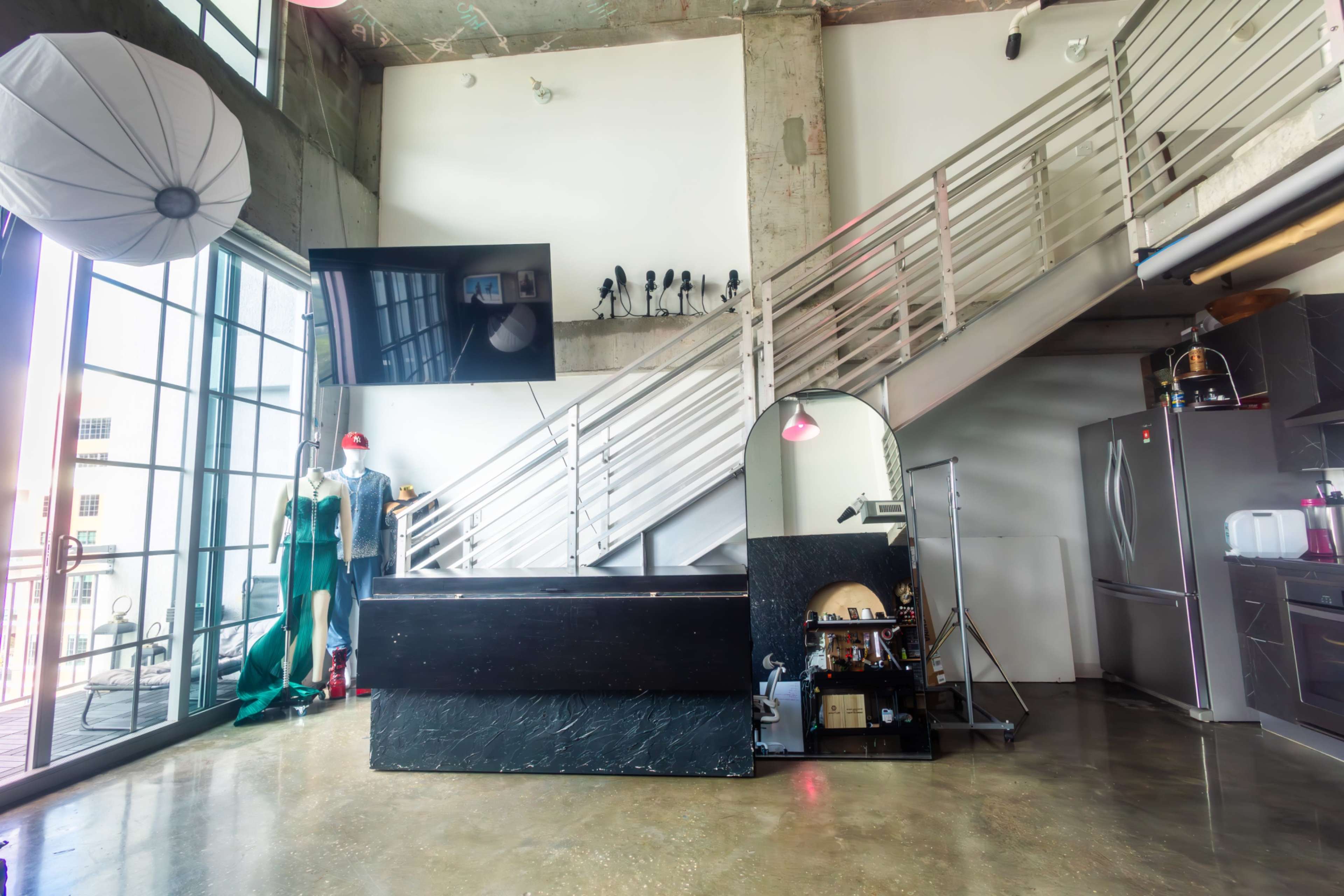 The image showcases a modern interior featuring a staircase, a flat-screen TV mounted on the wall, and various furniture and decor elements in an open space.