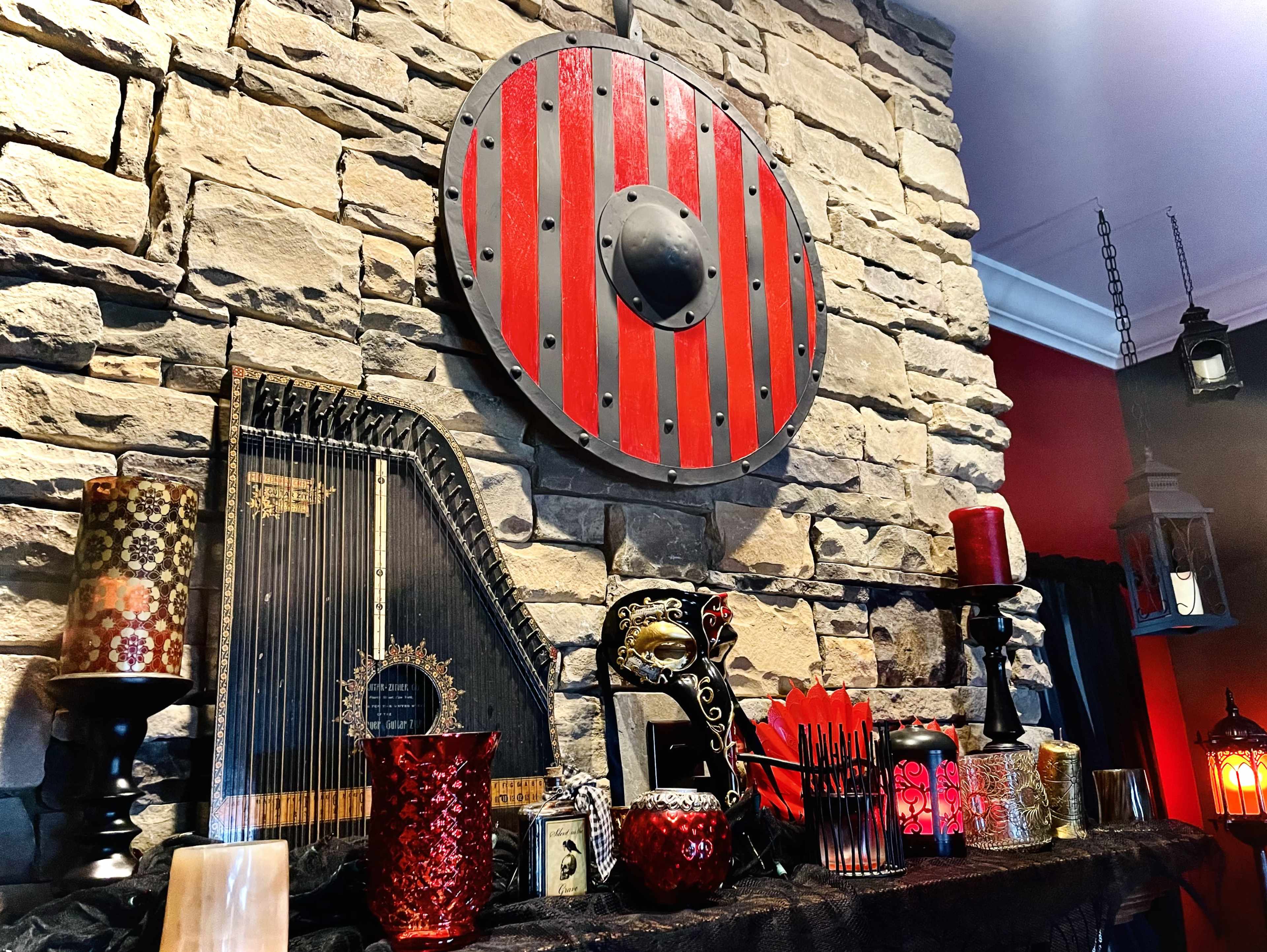 A stone wall displays a red and black shield above a collection of decorative items, including candles, a harplike instrument, and various lanterns.