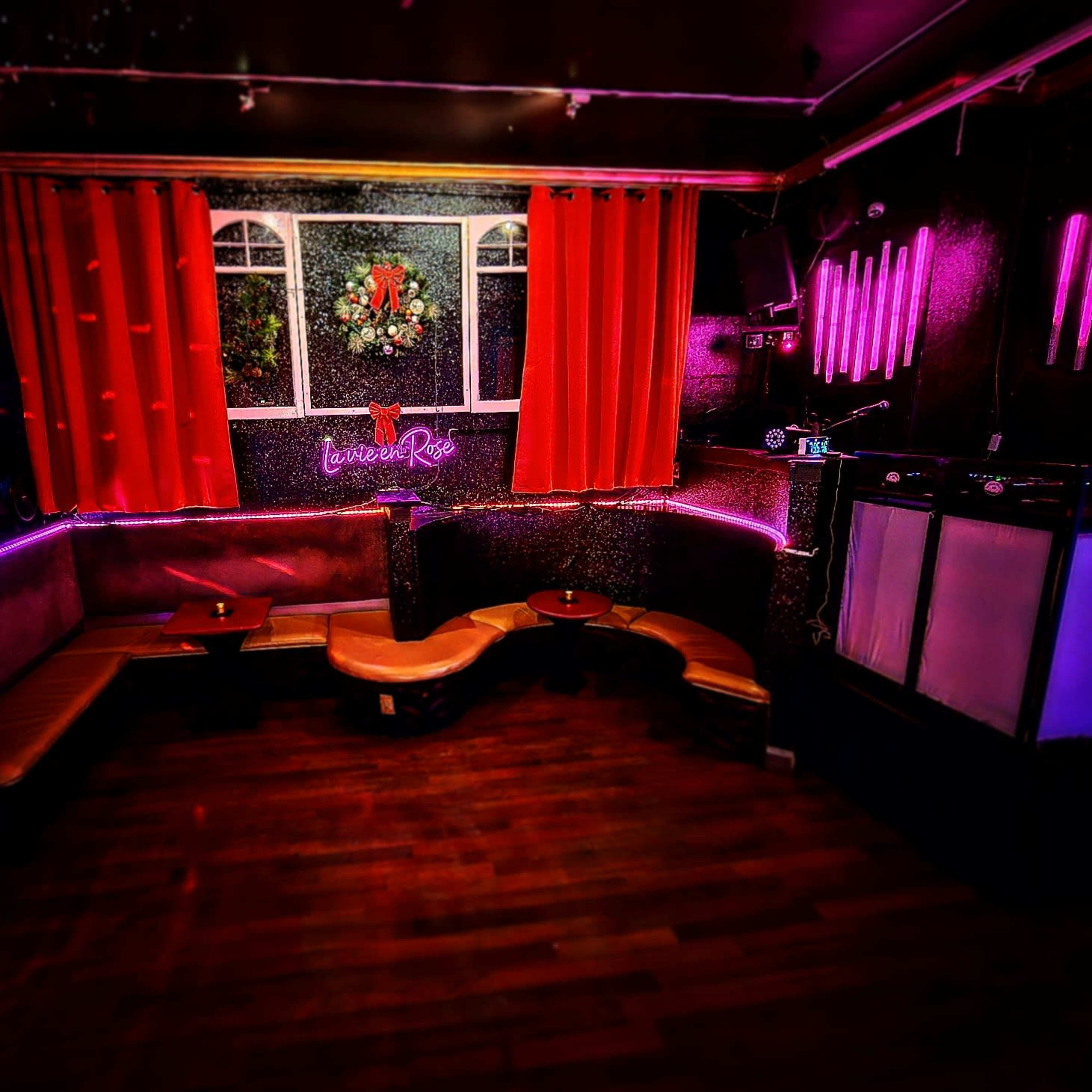 A dimly lit bar area with red curtains, a decorated wall, and neon lighting.