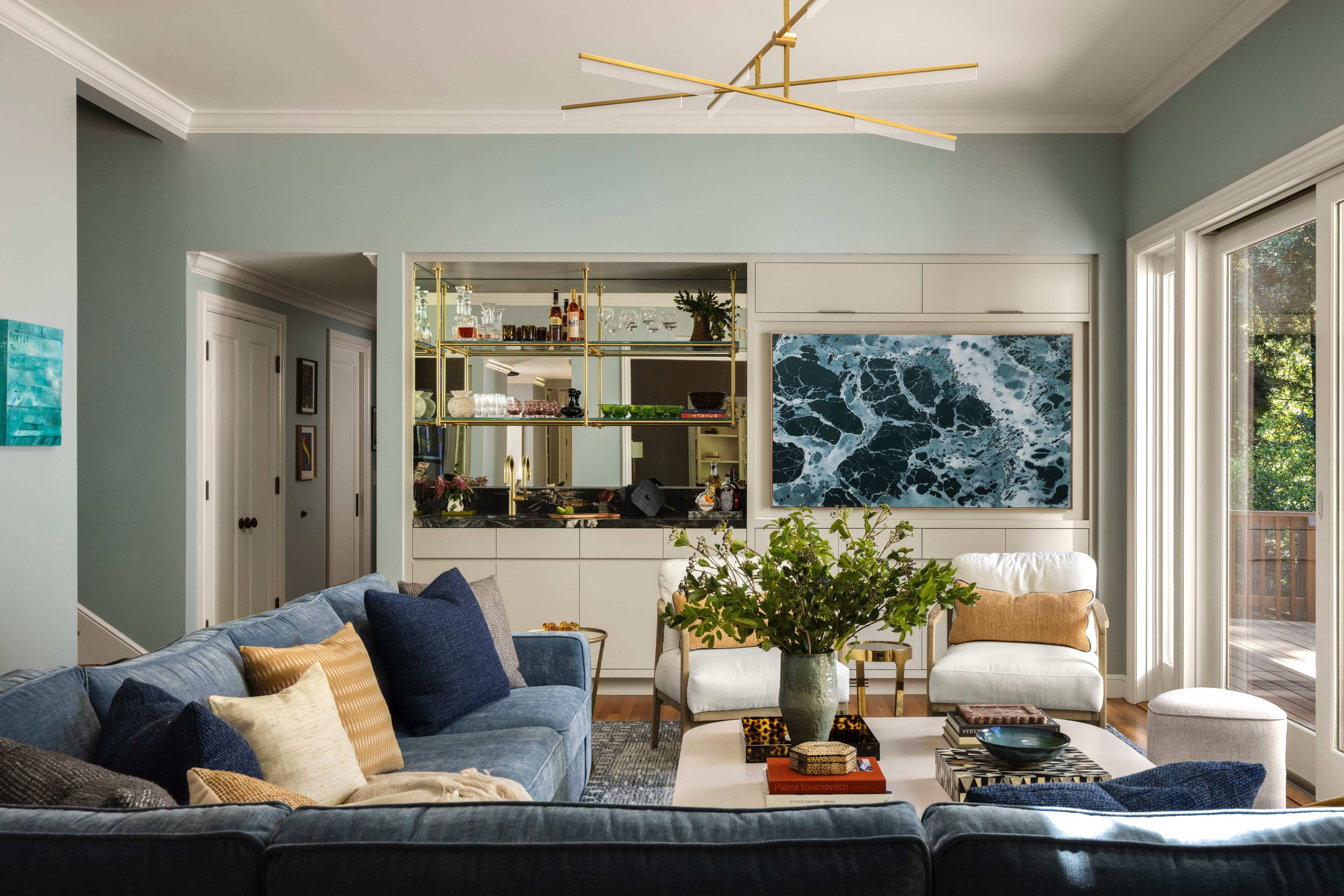 The living room features a blue sectional sofa, a coffee table with decorative items, and a wall unit displaying shelves and a large artwork depicting ocean waves.