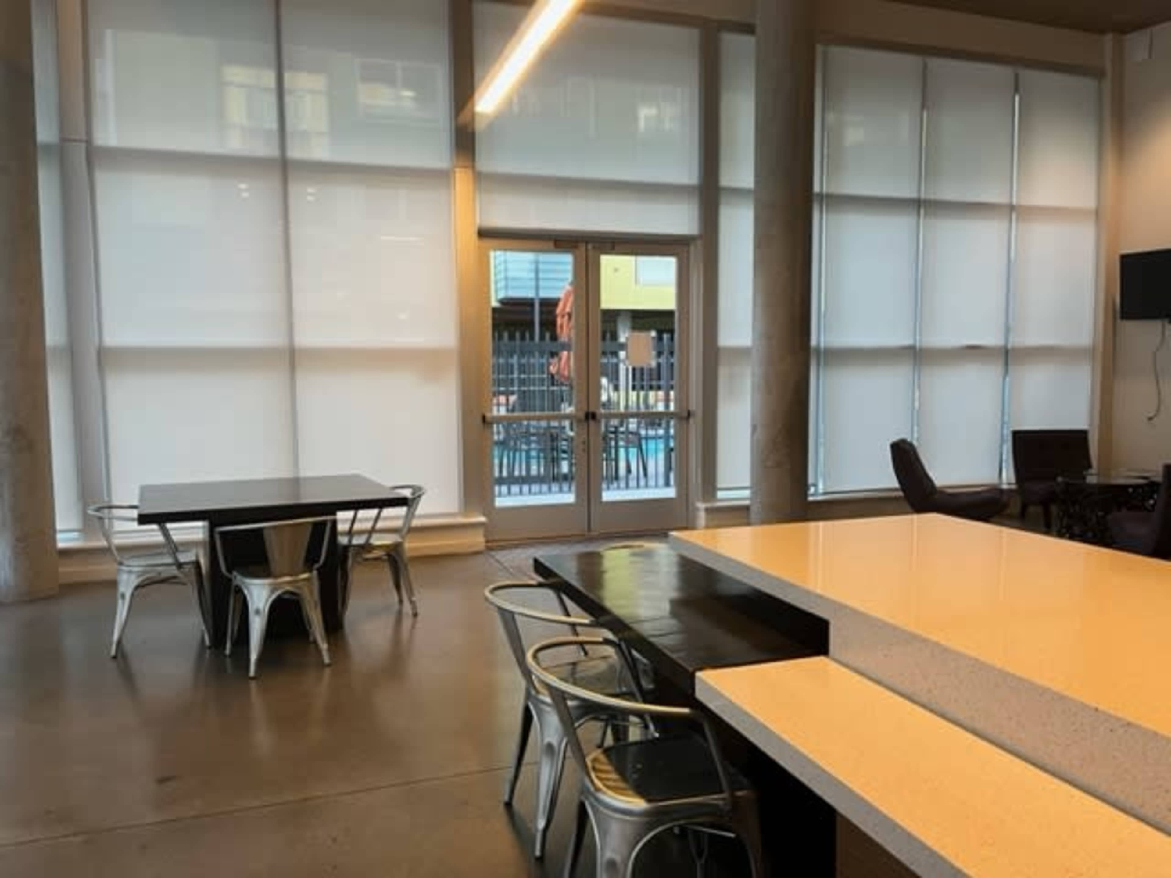 A modern, open space with large windows covered by sheer blinds, a table with metal chairs, and a countertop.
