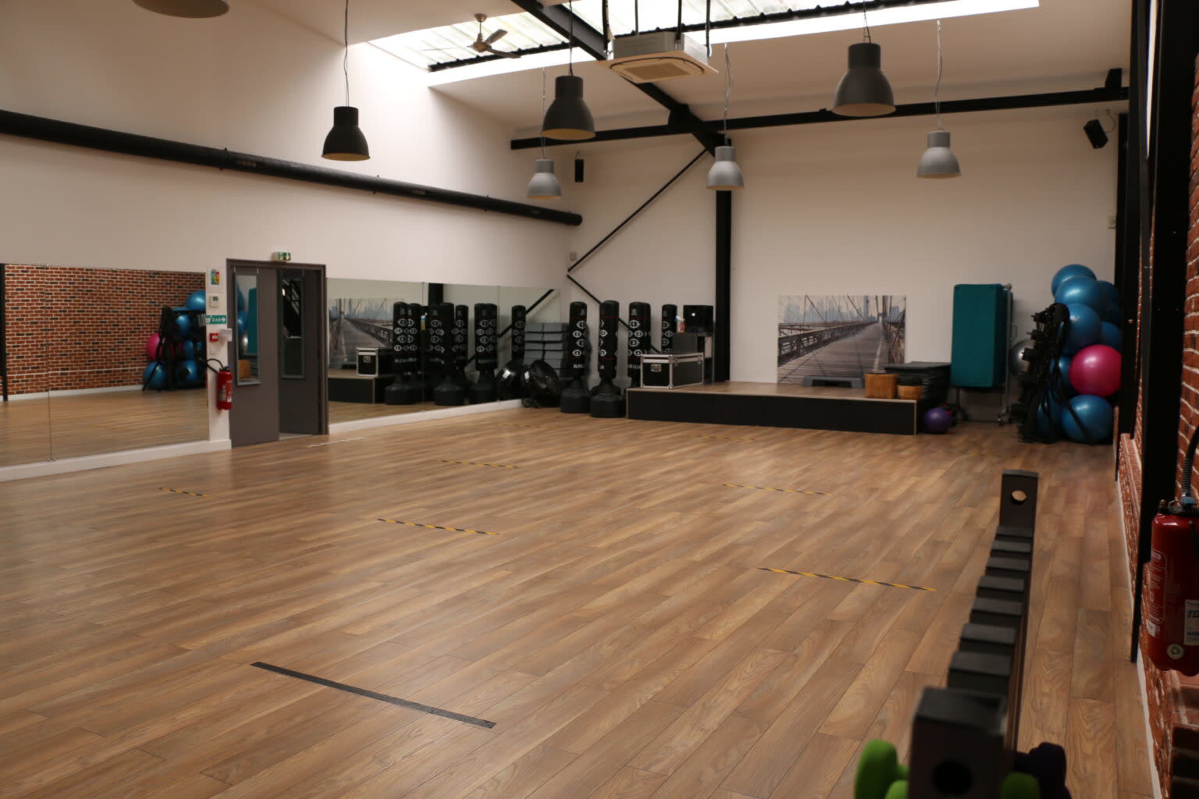 An empty fitness studio with wooden flooring, mirrors, and various workout equipment lined against the walls.