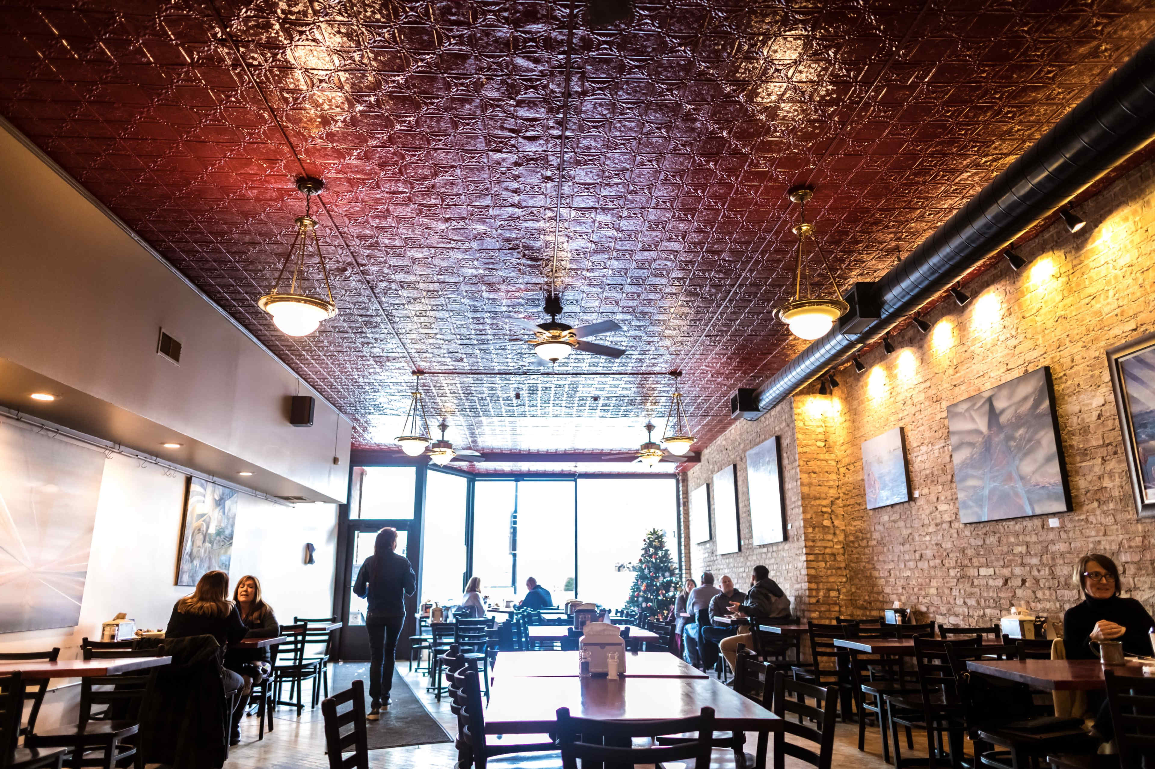 A cafe interior with wooden tables and chairs, a tin ceiling, and large windows letting in natural light.