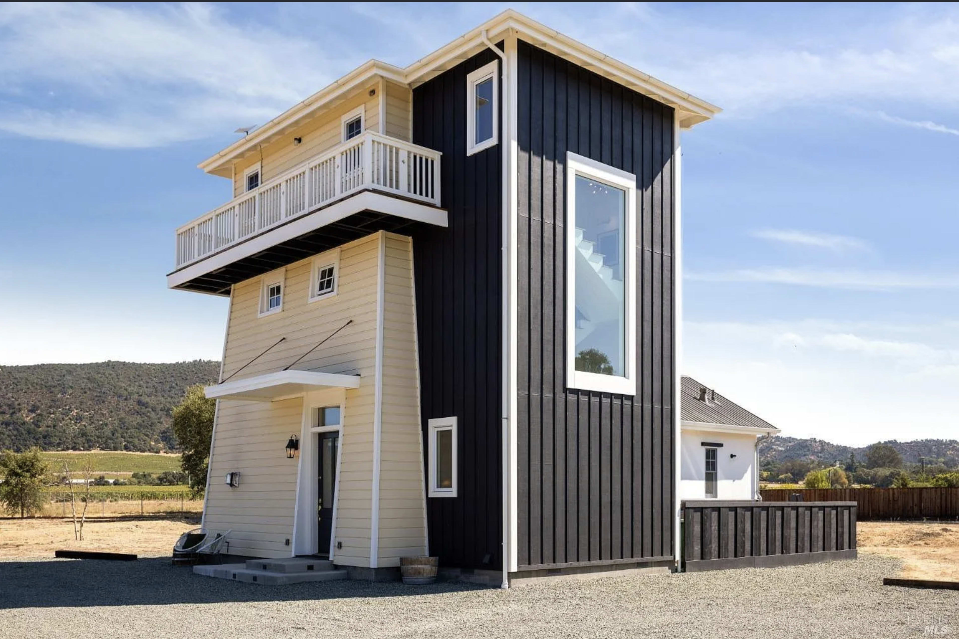 The image shows a modern two-story house with a distinctive architectural design, featuring a combination of black and white exterior finishes and a large window on the upper level.