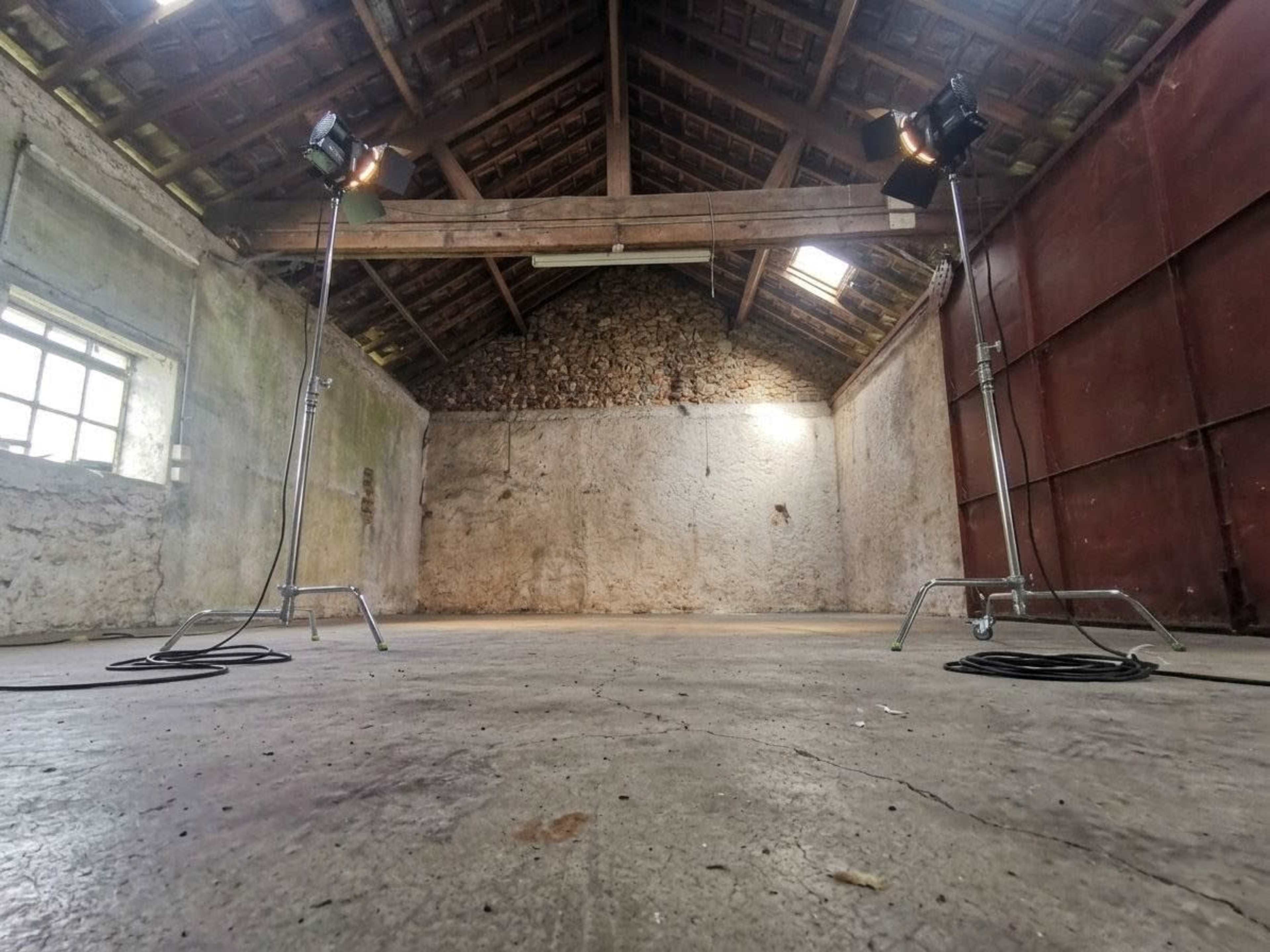 The image shows an empty, rustic interior of a room with bare stone walls and two studio lights positioned on stands.