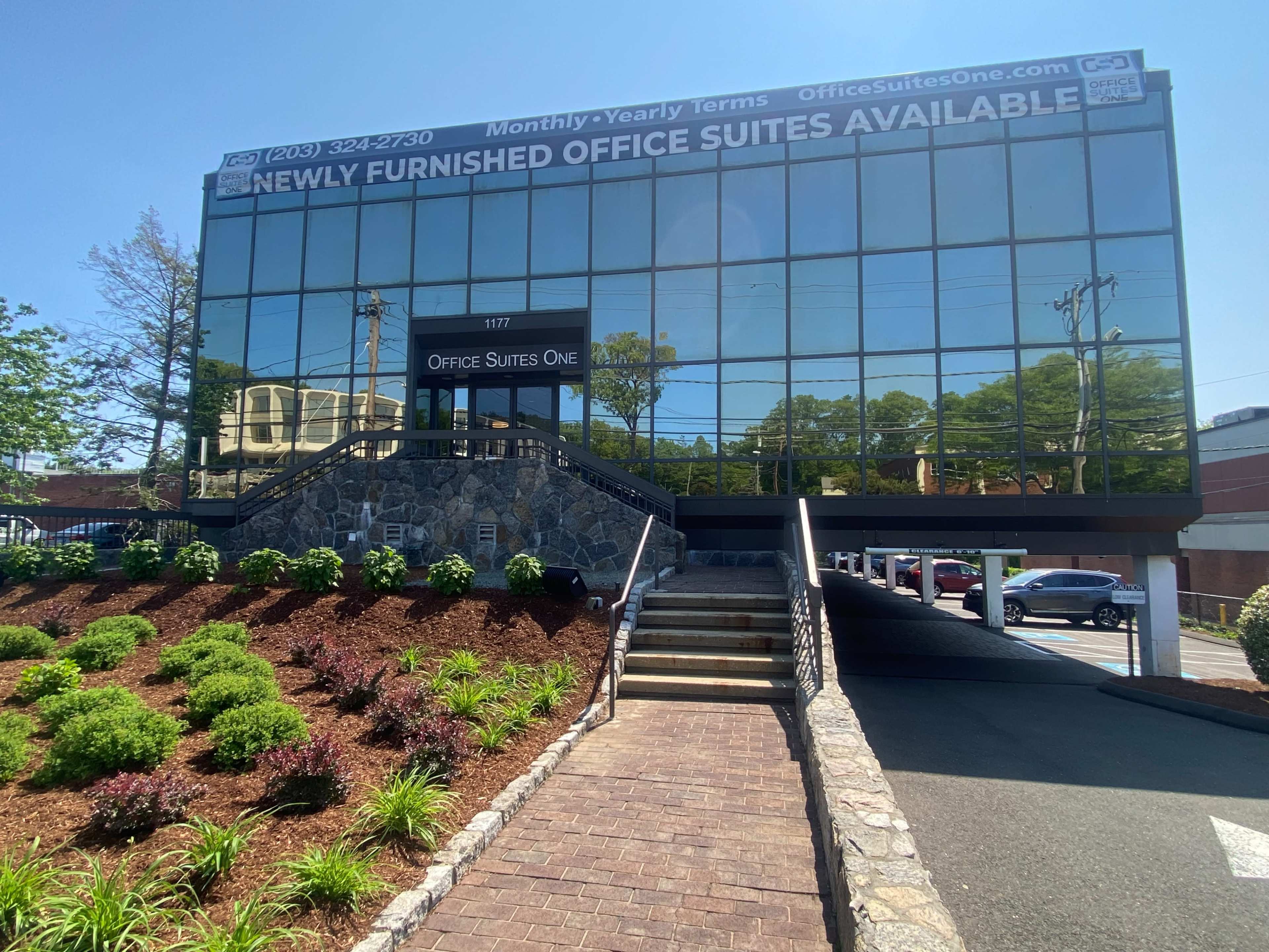 A modern glass building with a stairway leading up to its entrance, advertising newly furnished office suites available for lease.
