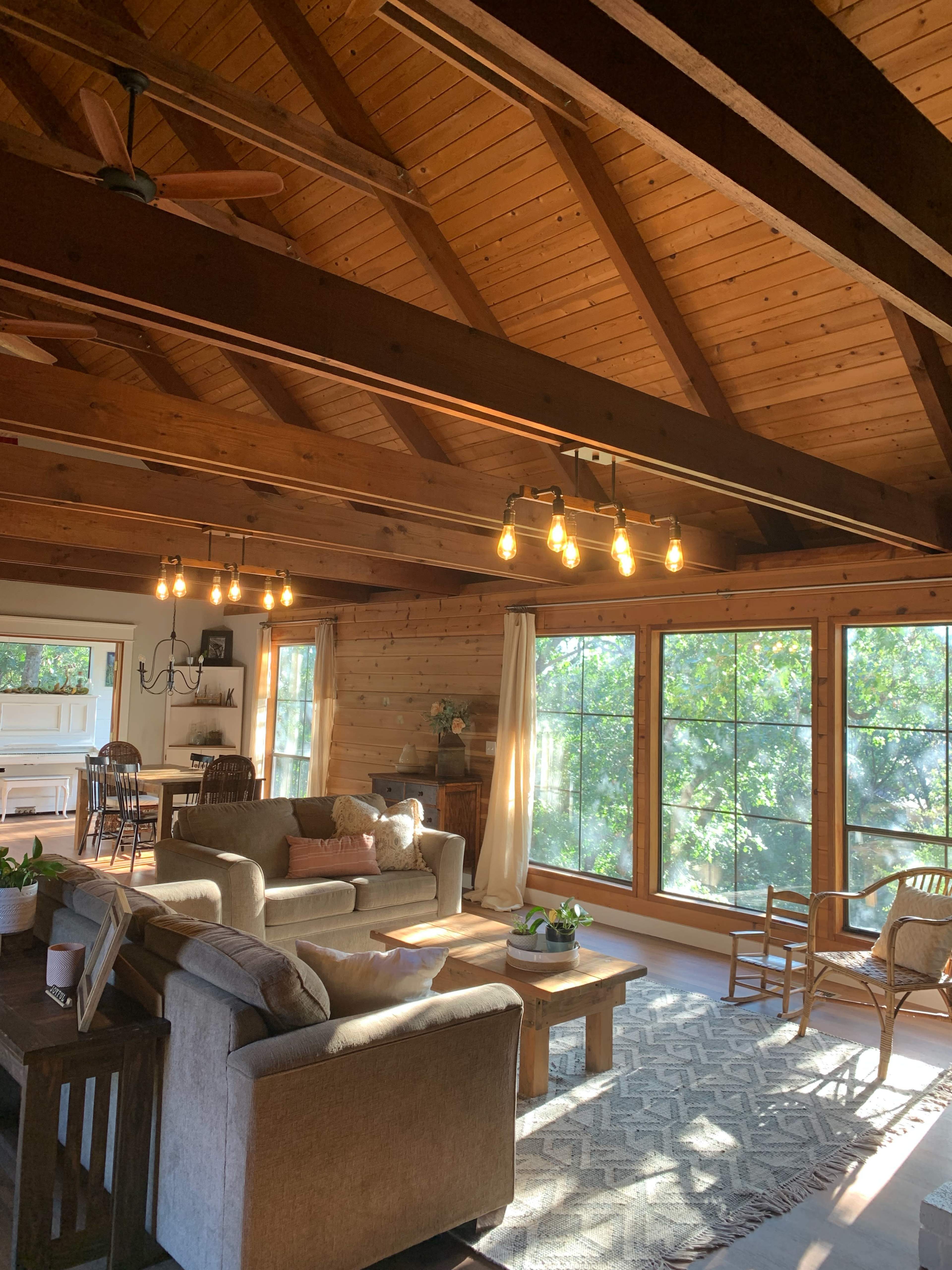 A rustic living room with wooden walls, a high ceiling, large windows, and a cozy seating arrangement.