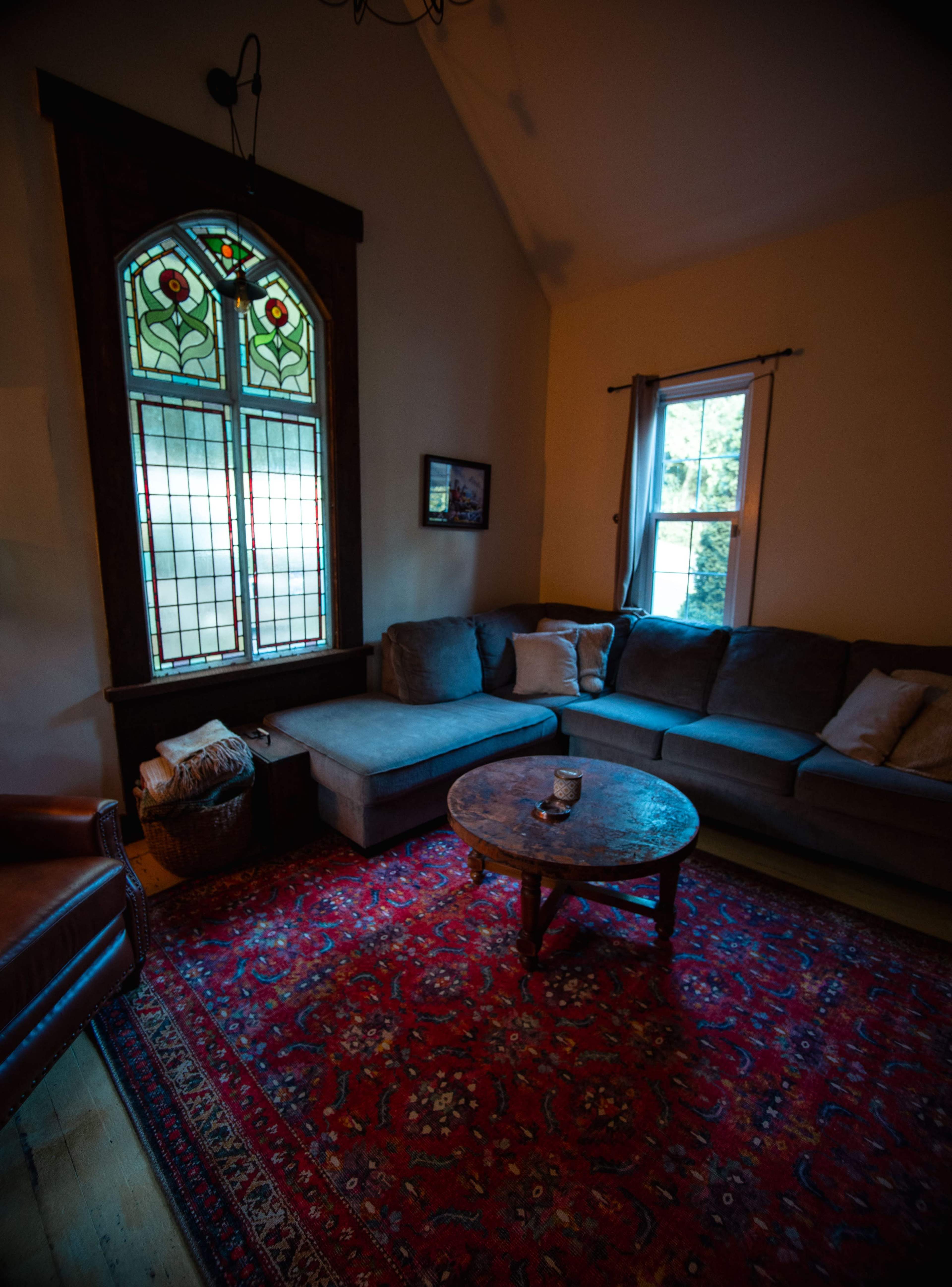 A cozy living room features a large sectional couch, a round coffee table, and a colorful stained glass window.