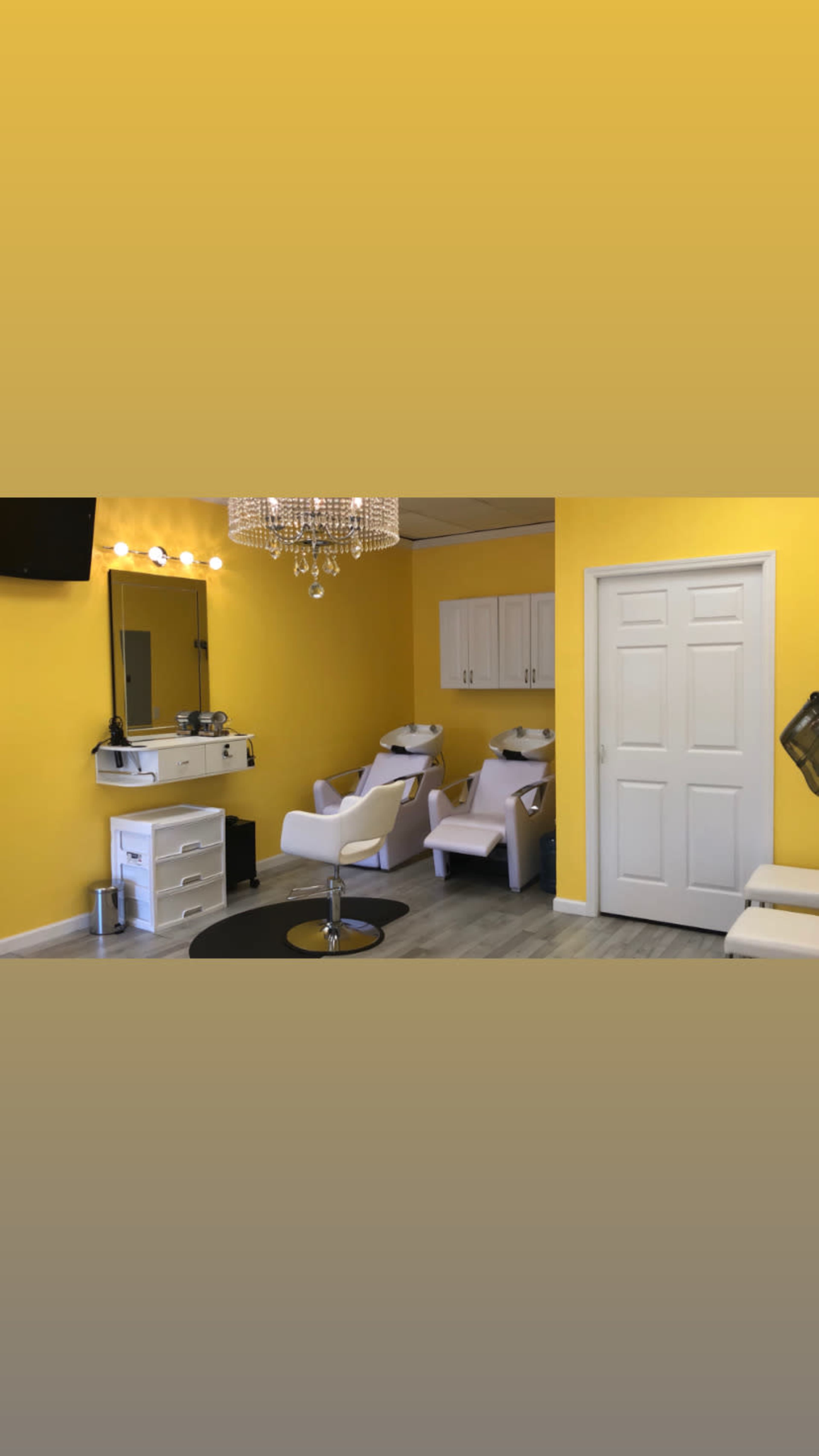 A brightly colored yellow salon interior featuring white furniture, a mirror with lights, and a chandelier.