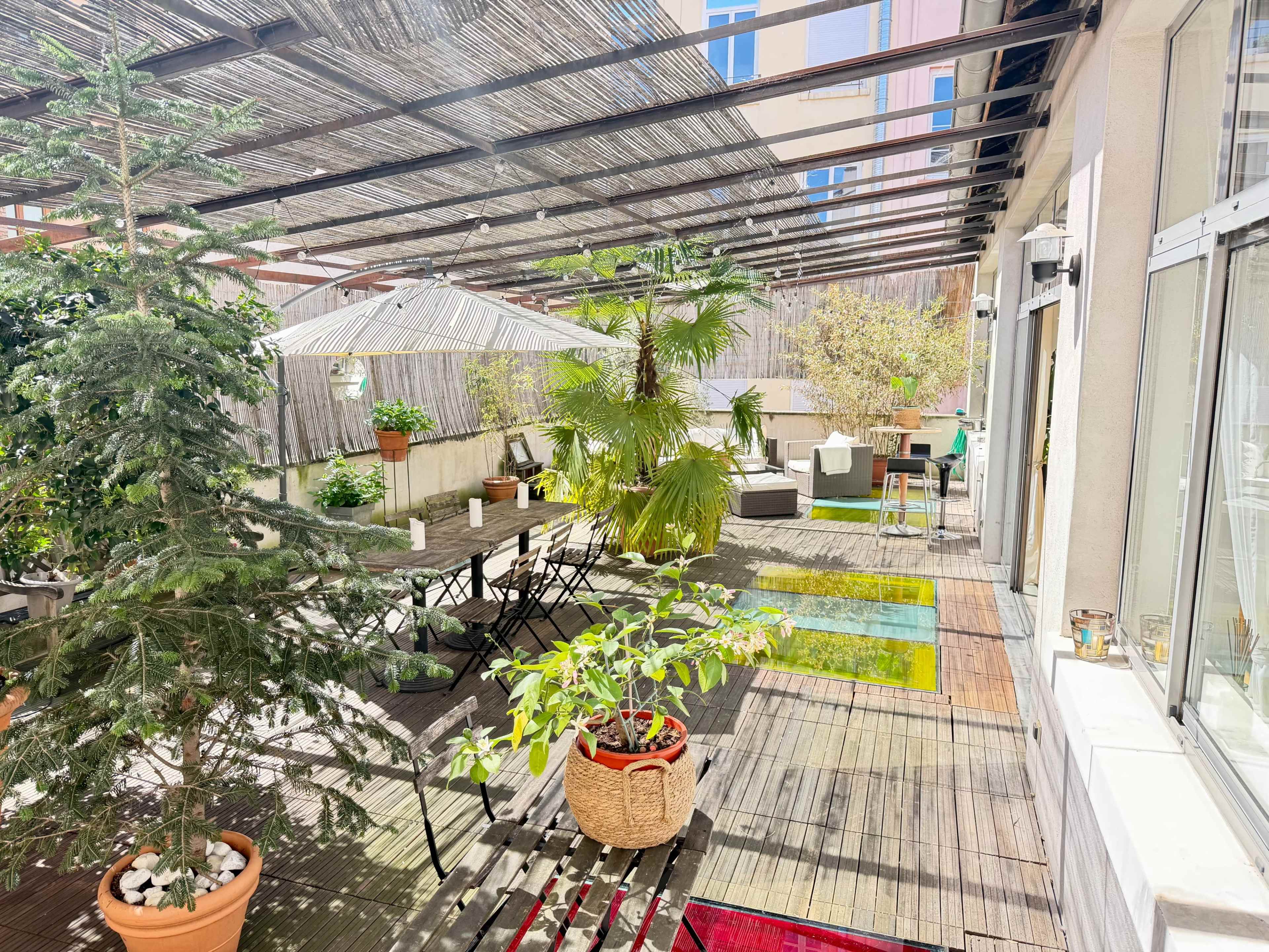The image shows a spacious rooftop terrace with various plants, outdoor furniture, and a sunshade.