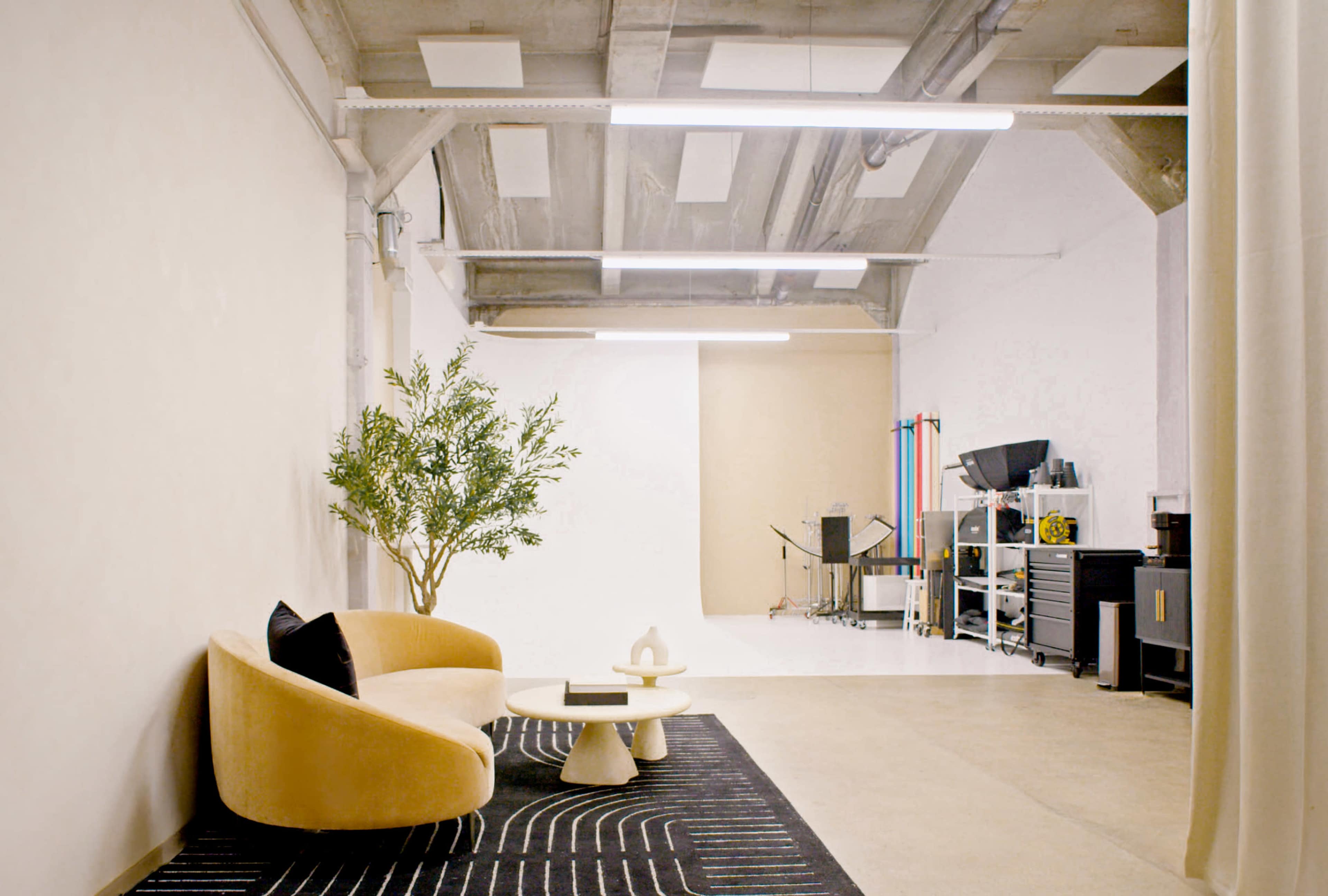 The image features a modern studio space with a minimalist design, including a curved sofa, a small table, and a backdrop area for photography or videography.