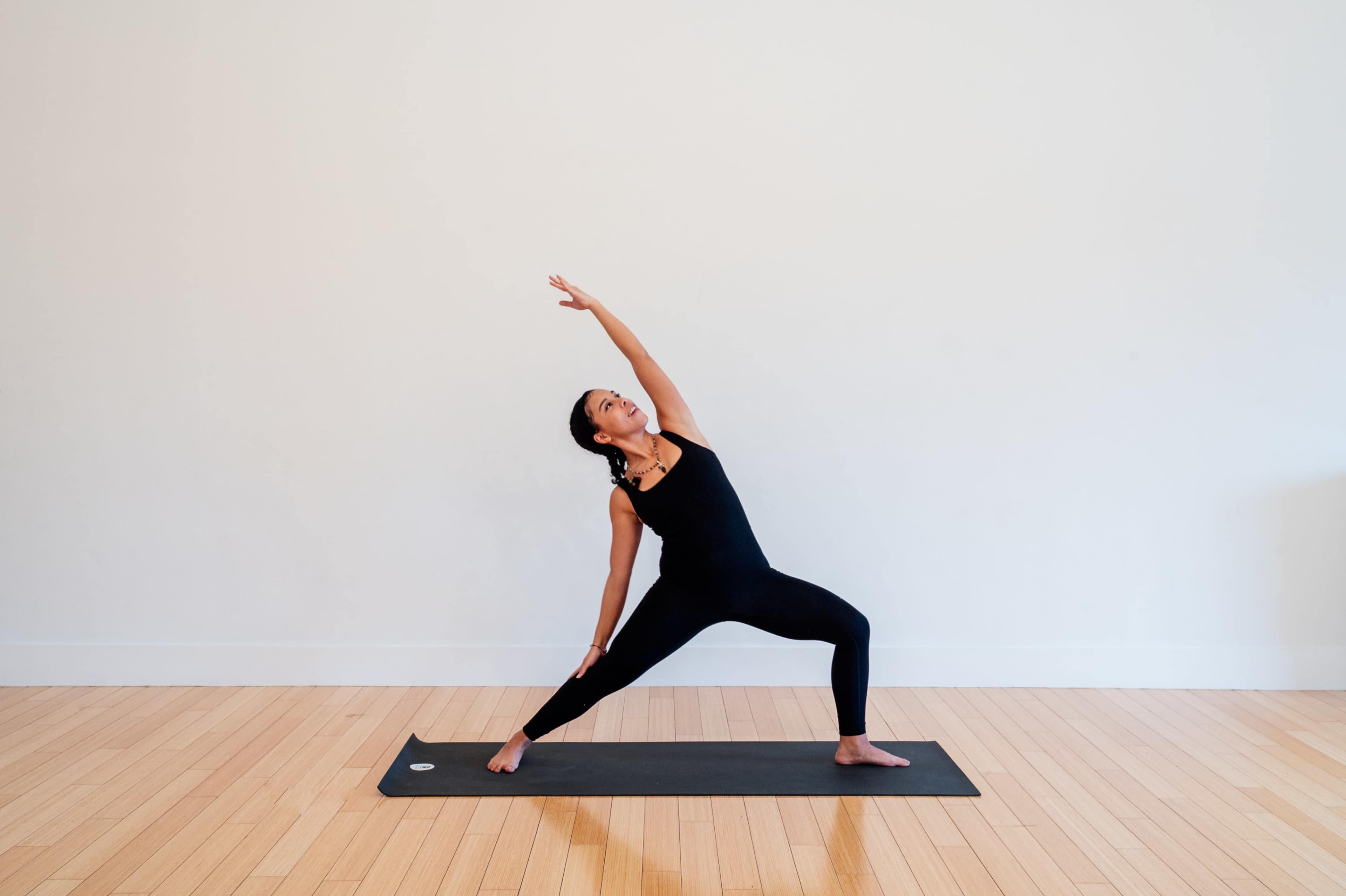 A woman performs a yoga pose on a mat in a spacious, minimally decorated room with wooden floors.