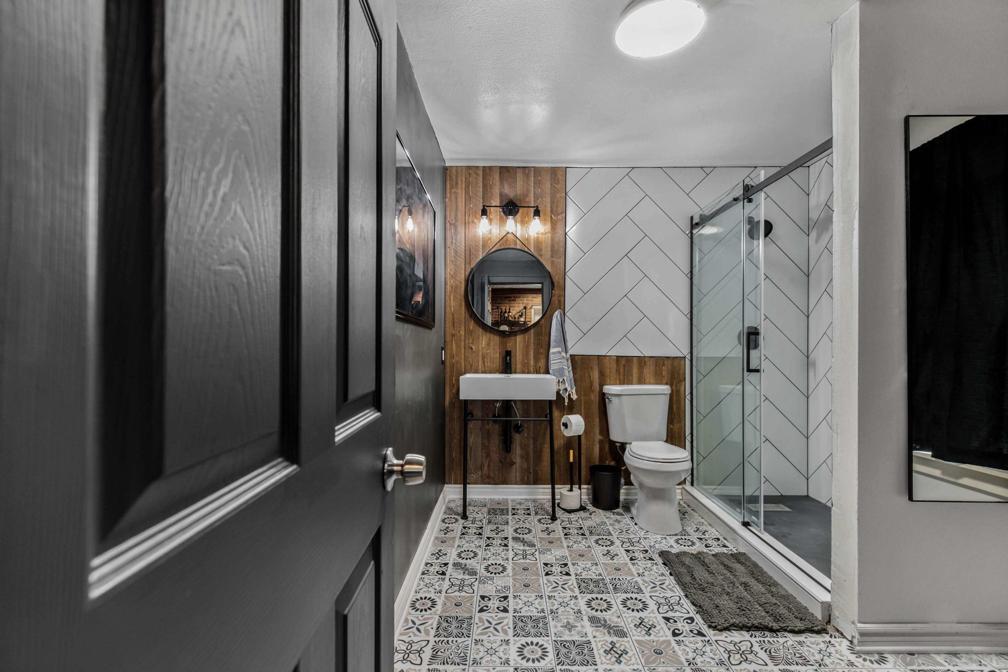 A modern bathroom with a shower, a toilet, a sink, and patterned tile flooring.