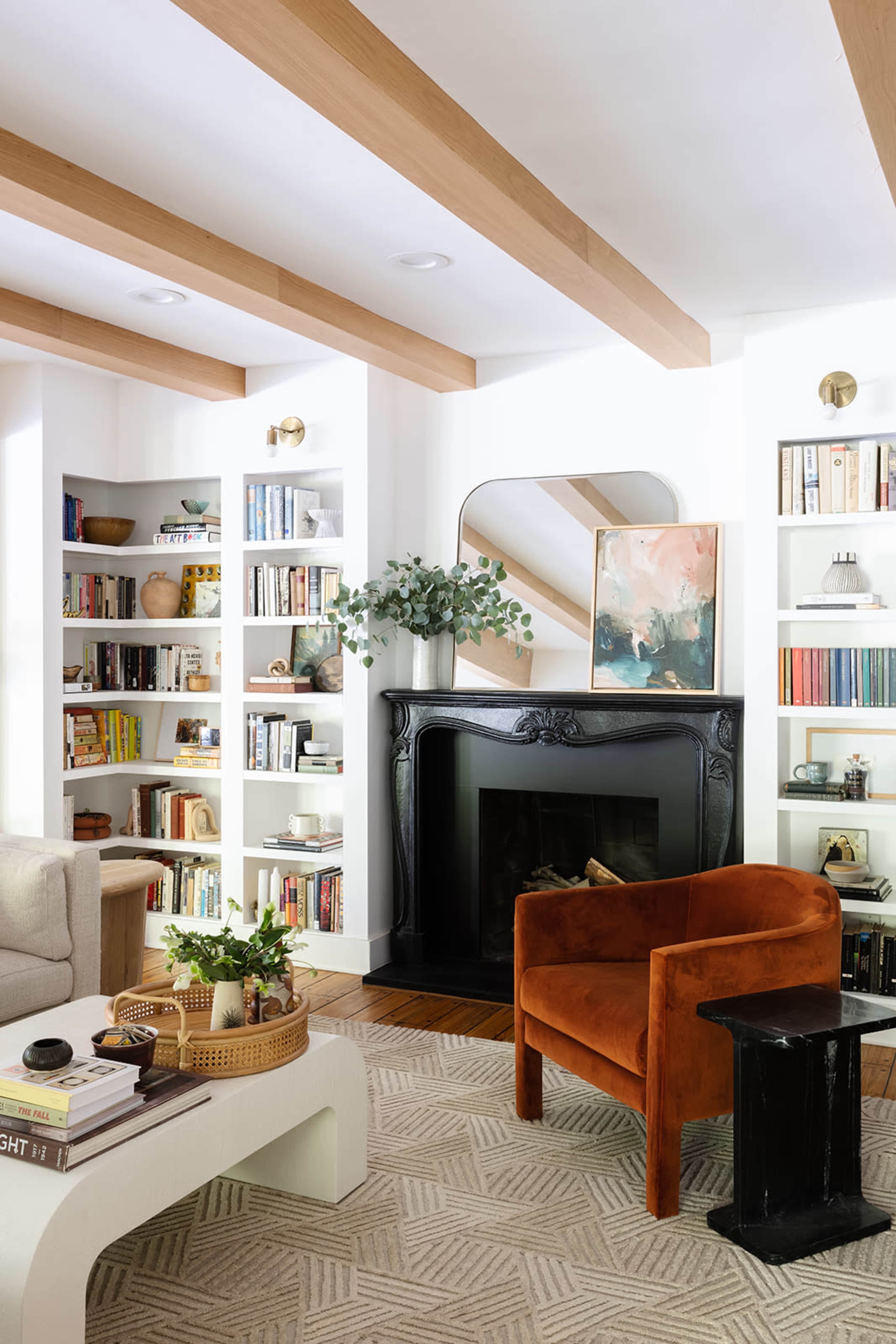 A cozy living room features a black fireplace, bookshelves filled with books and decor, a brown armchair, and a modern coffee table.