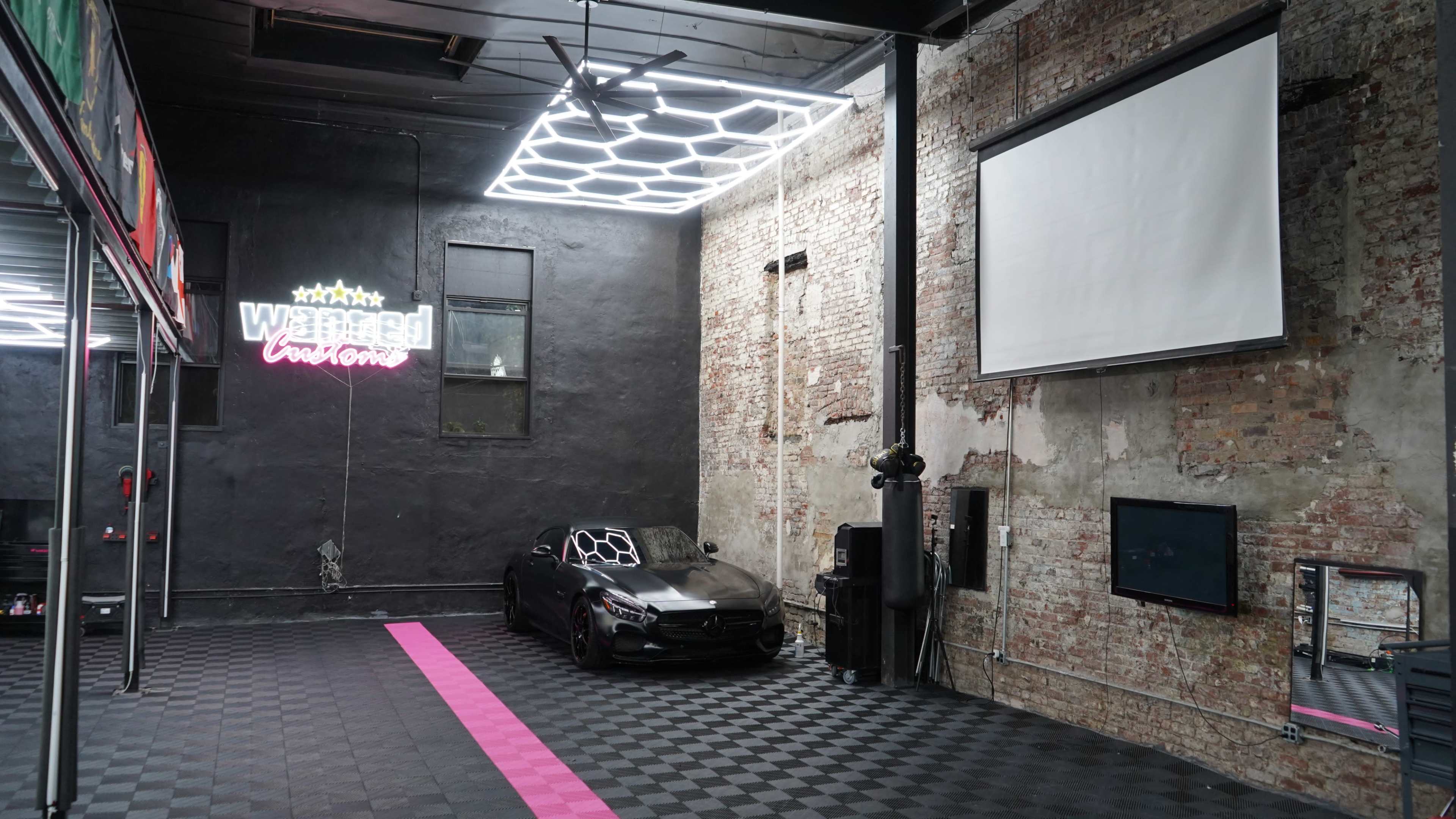 The interior of a car detailing shop features a black sports car, exposed brick walls, and modern lighting.