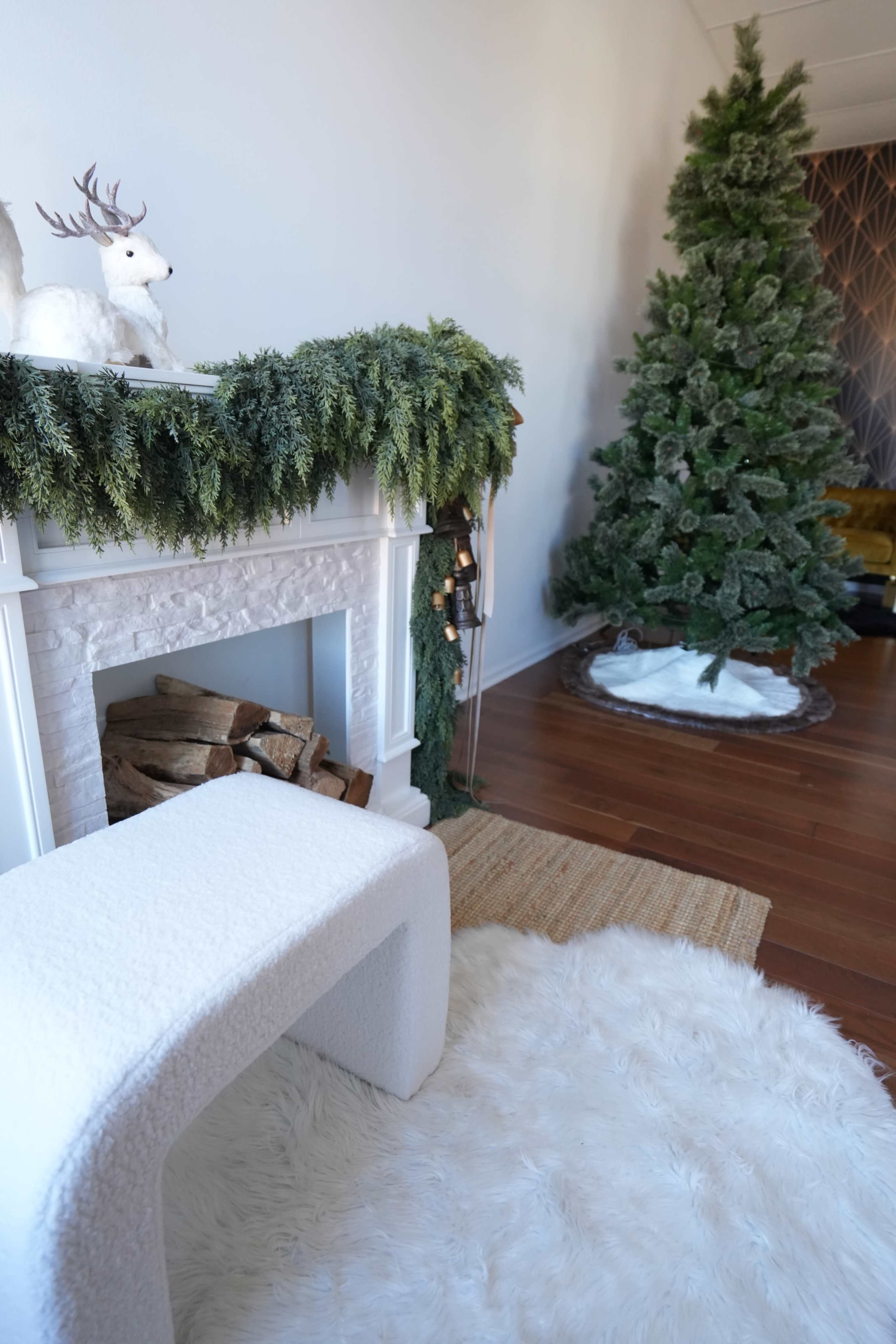 A white faux fur rug lies on the floor in front of a decorated fireplace, while a Christmas tree stands in the corner, adorned with greenery and lights.