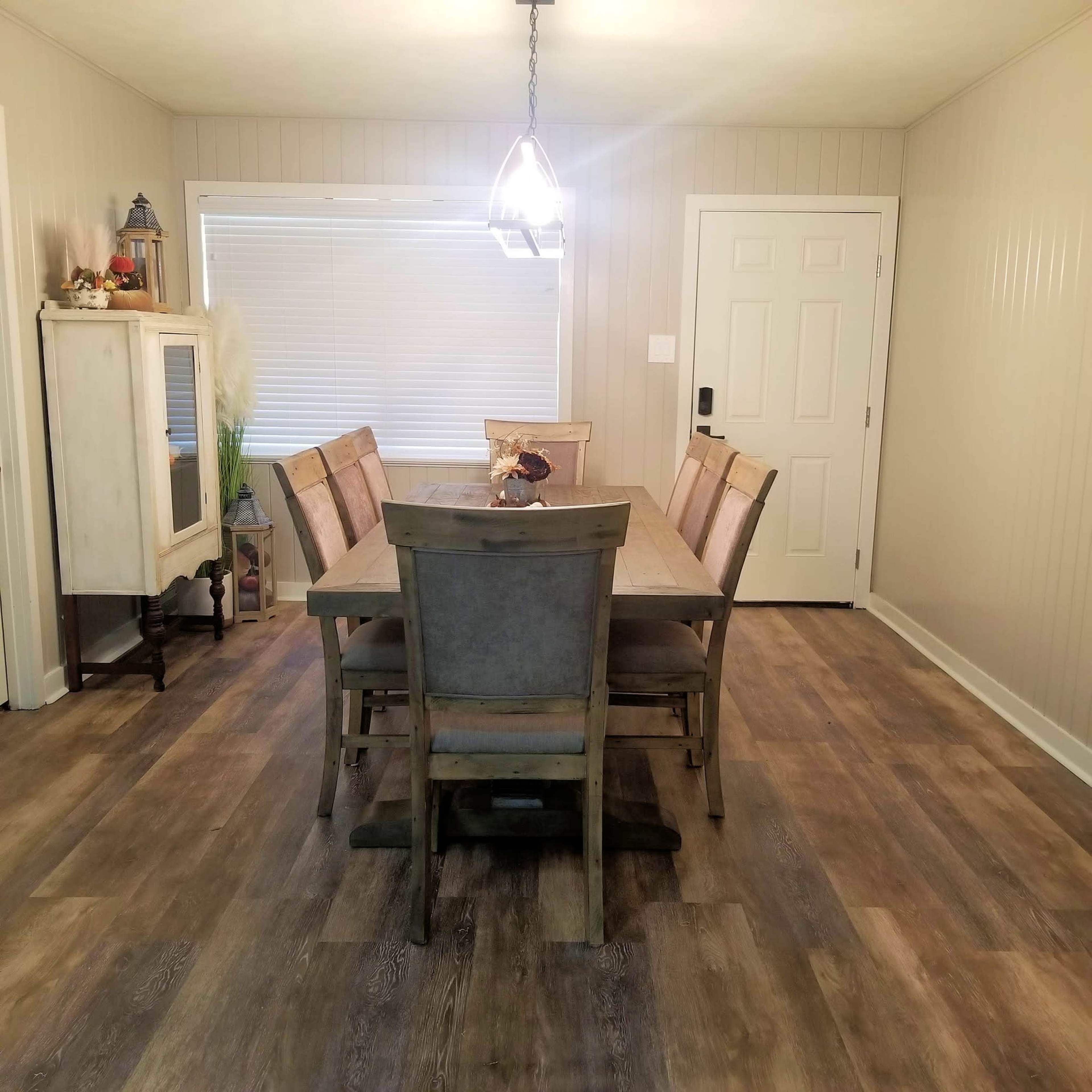 A wooden dining table with eight chairs is set in a room with light-colored walls and a door leading outside.