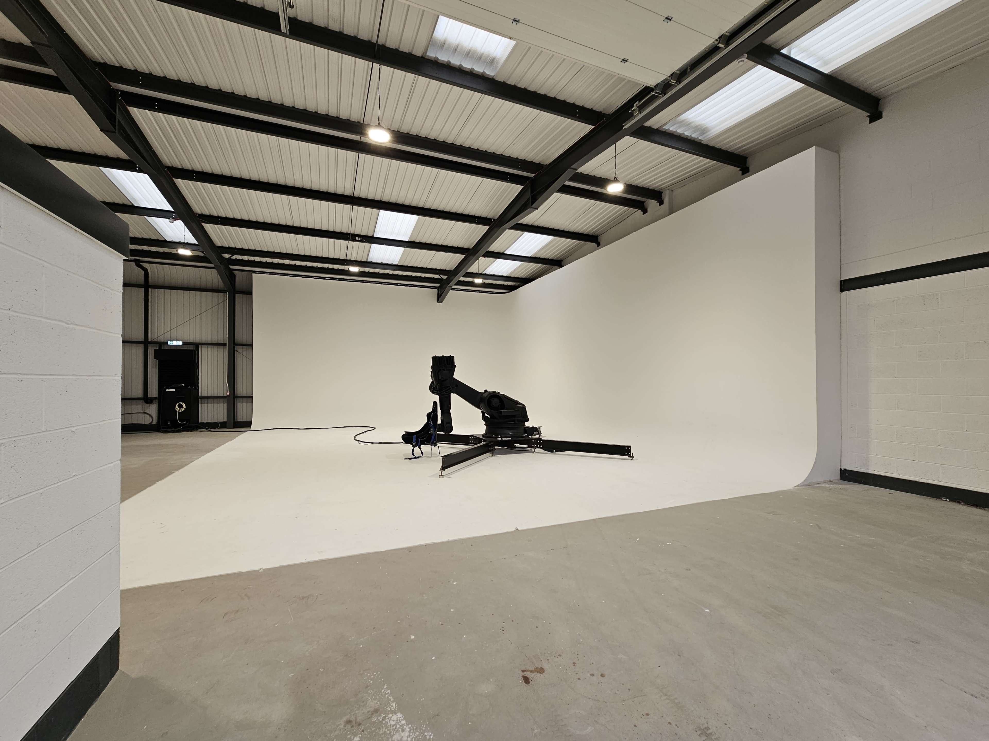 A spacious studio features a large white backdrop and a stand for equipment in the center.