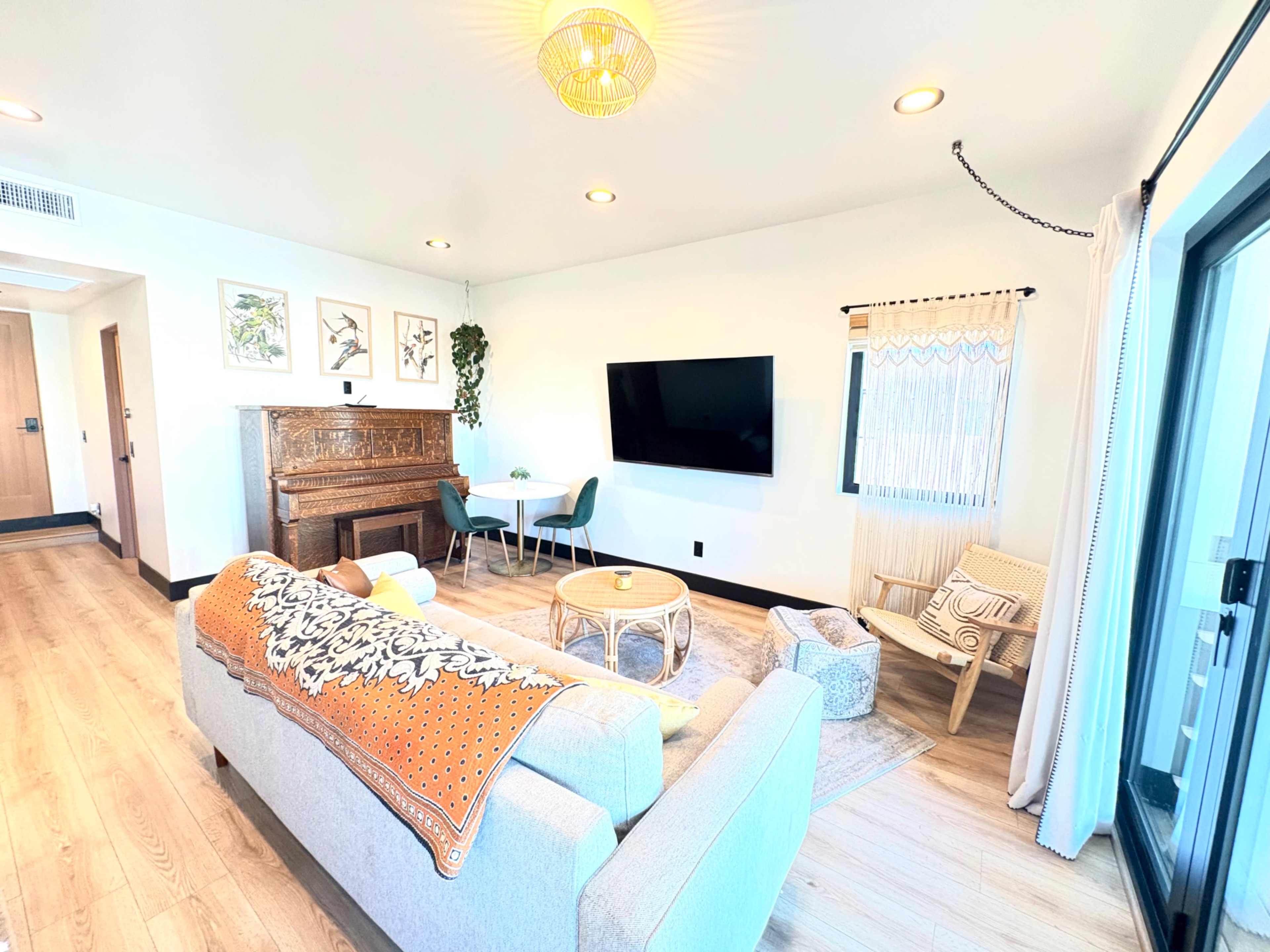 The image shows a modern living room with a light-colored sofa, a wooden cabinet, a wall-mounted TV, and various seating arrangements alongside a small dining table.