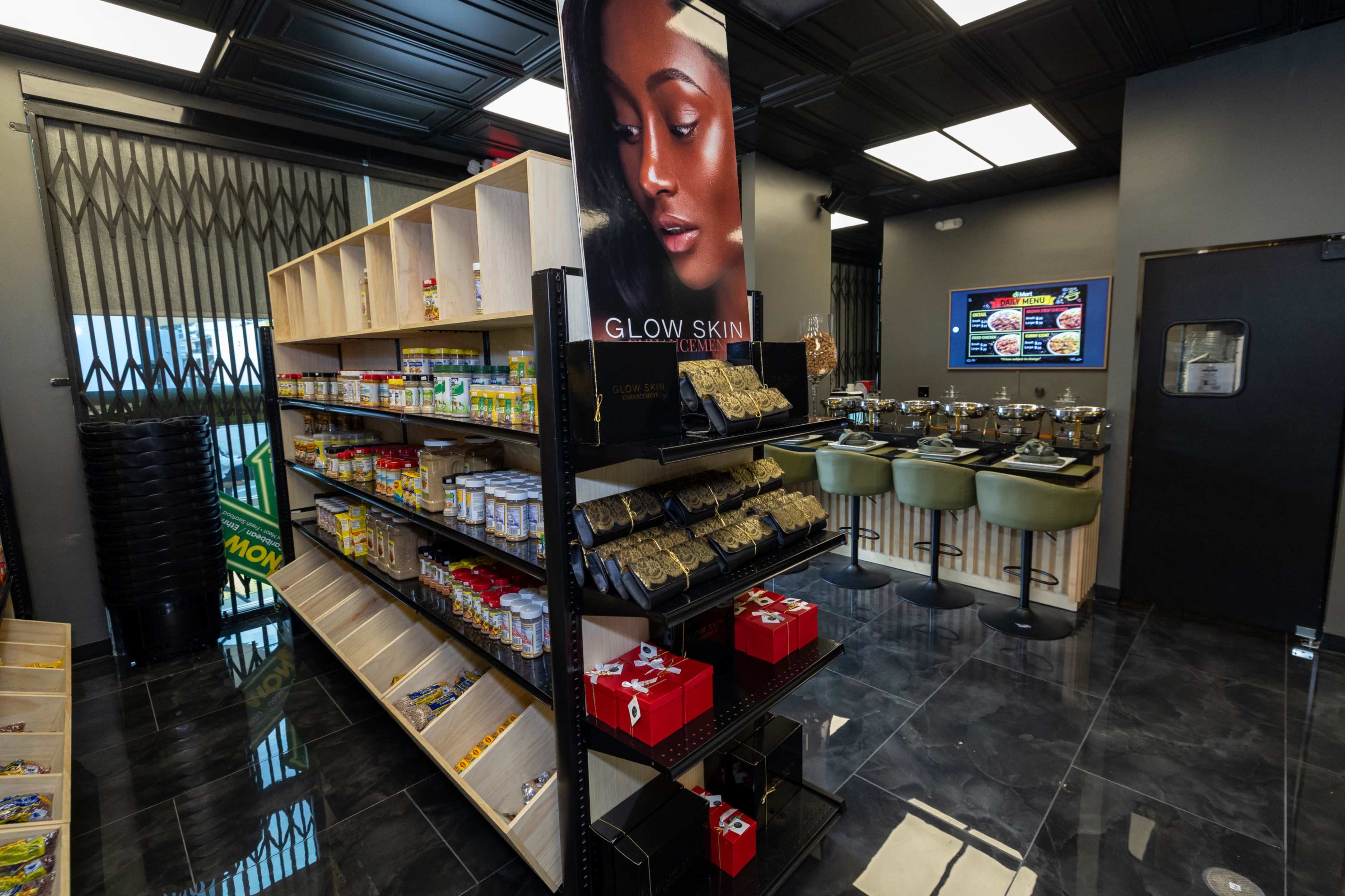 The image shows an interior of a convenience store with shelves stocked with various products, a promotional display for skincare, and a small seating area in the background.