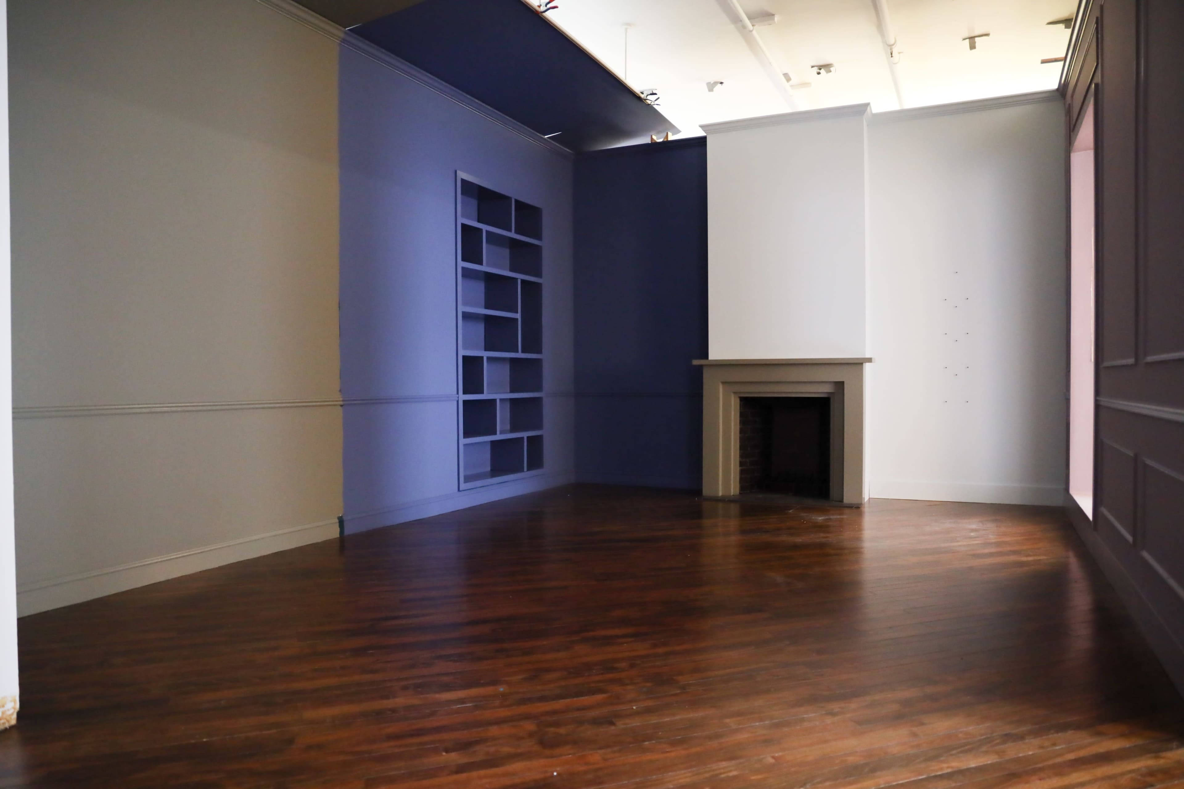 An empty room with hardwood flooring, featuring walls painted in various shades of gray and blue, and a fireplace against one wall.