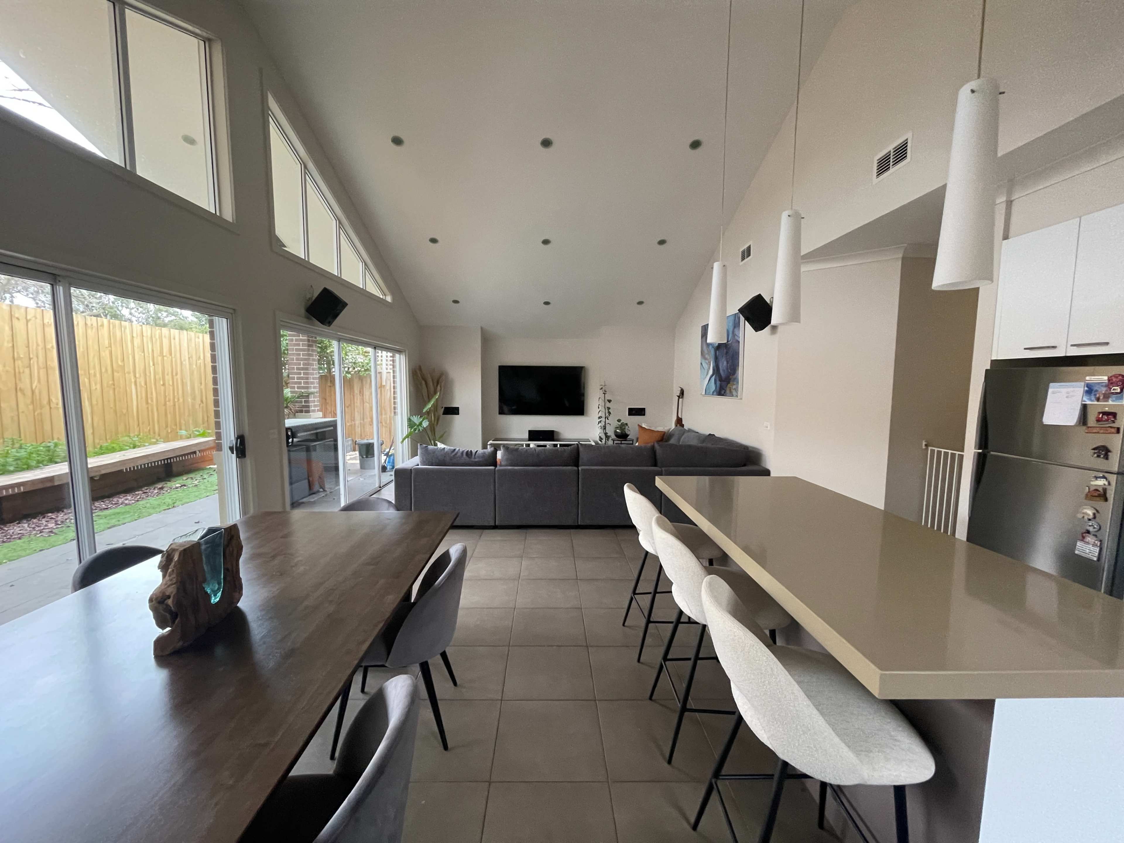 A modern open-concept living area with a kitchen bar, dining table, and a lounge space featuring a television.