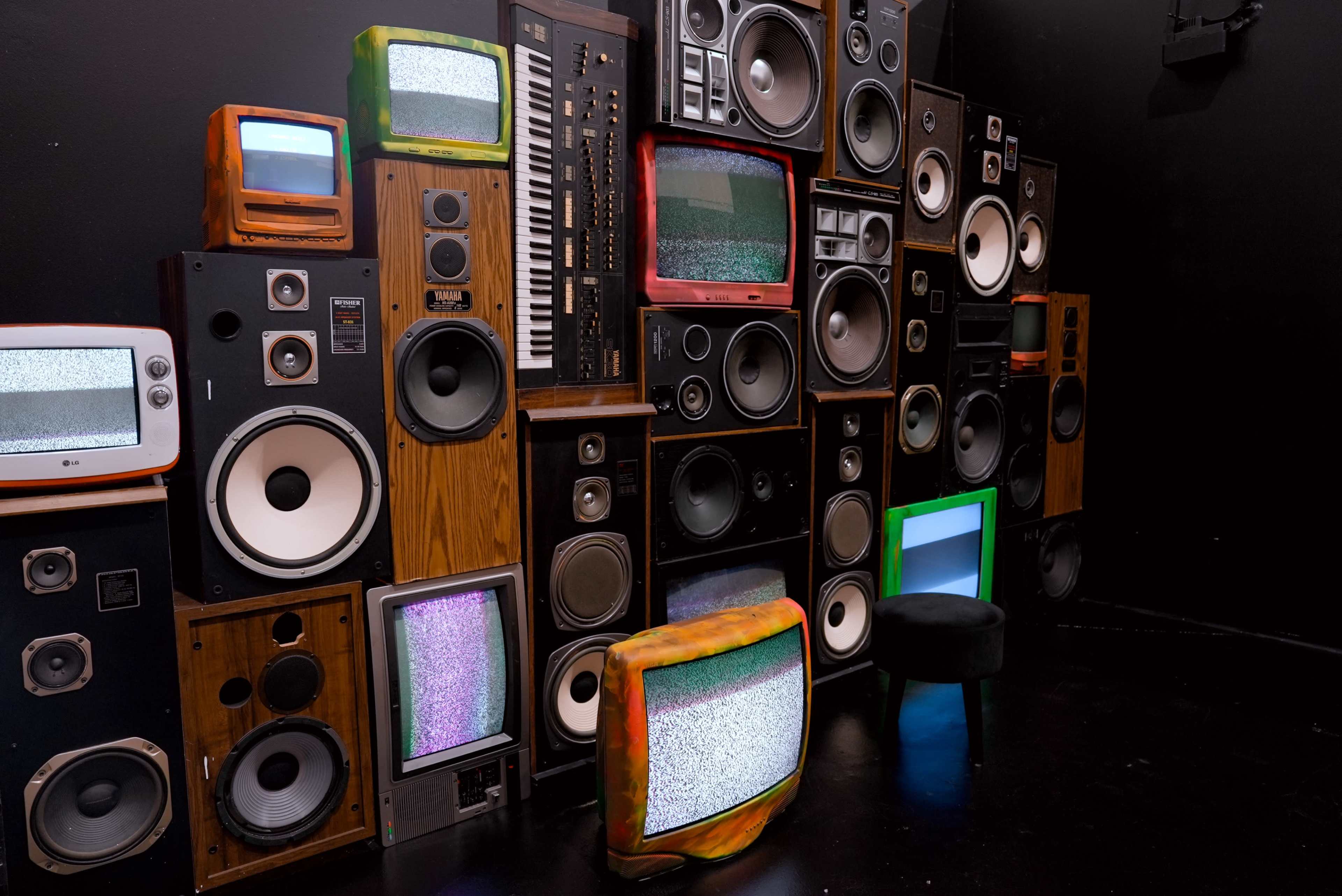 The image features a wall of vintage televisions and speakers arranged in a collage against a black background.
