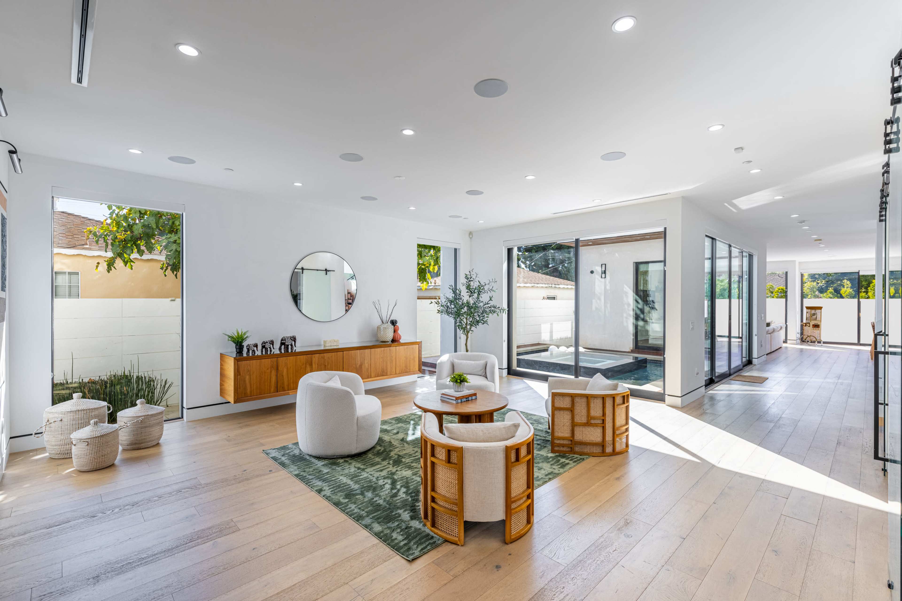 A spacious, modern living area featuring a round coffee table, four chairs, a large mirror on the wall, and glass doors leading to an outdoor space.