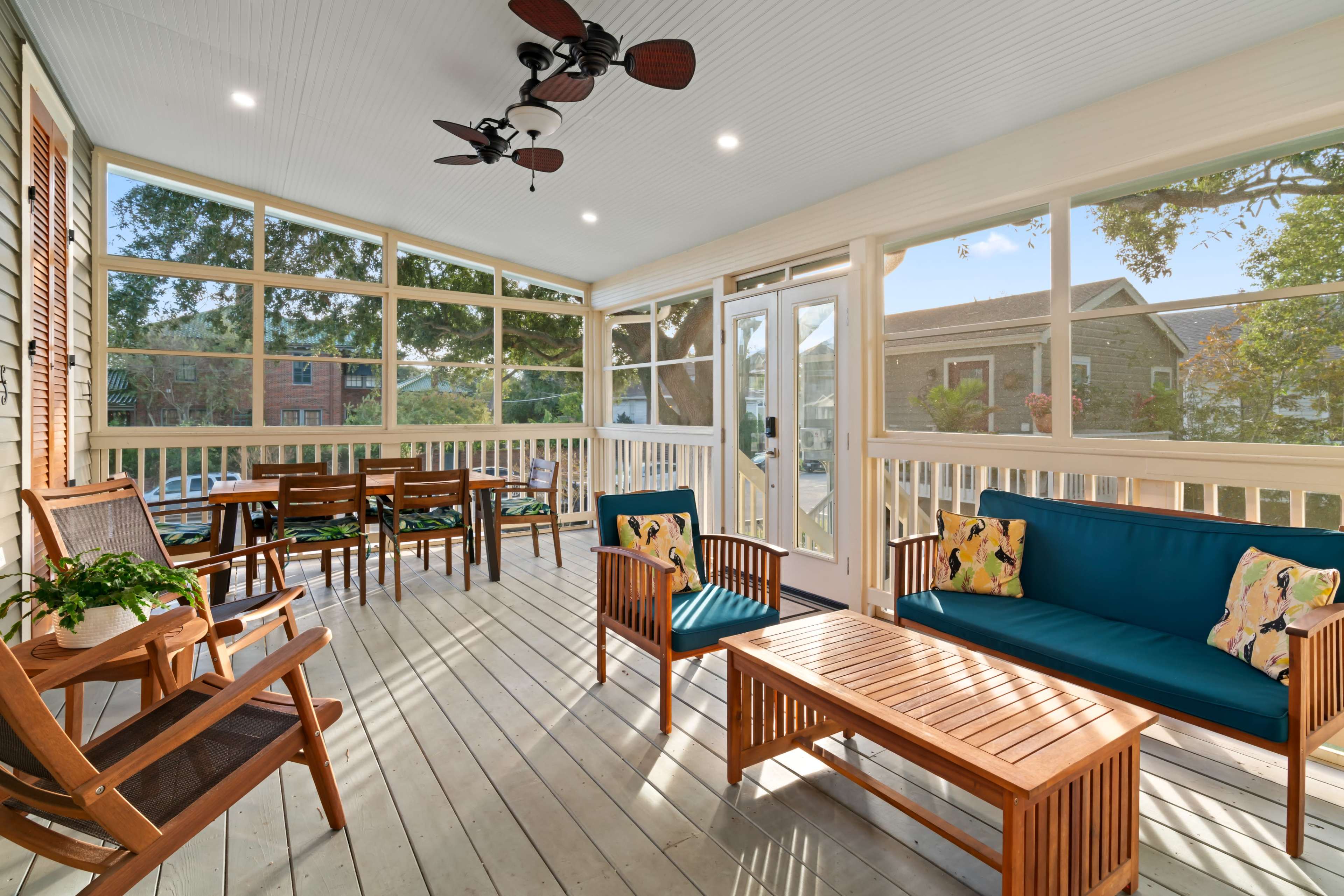 The image shows a spacious, screened-in porch featuring wooden furniture, including a seating area with blue cushions and a dining area with a table and chairs.
