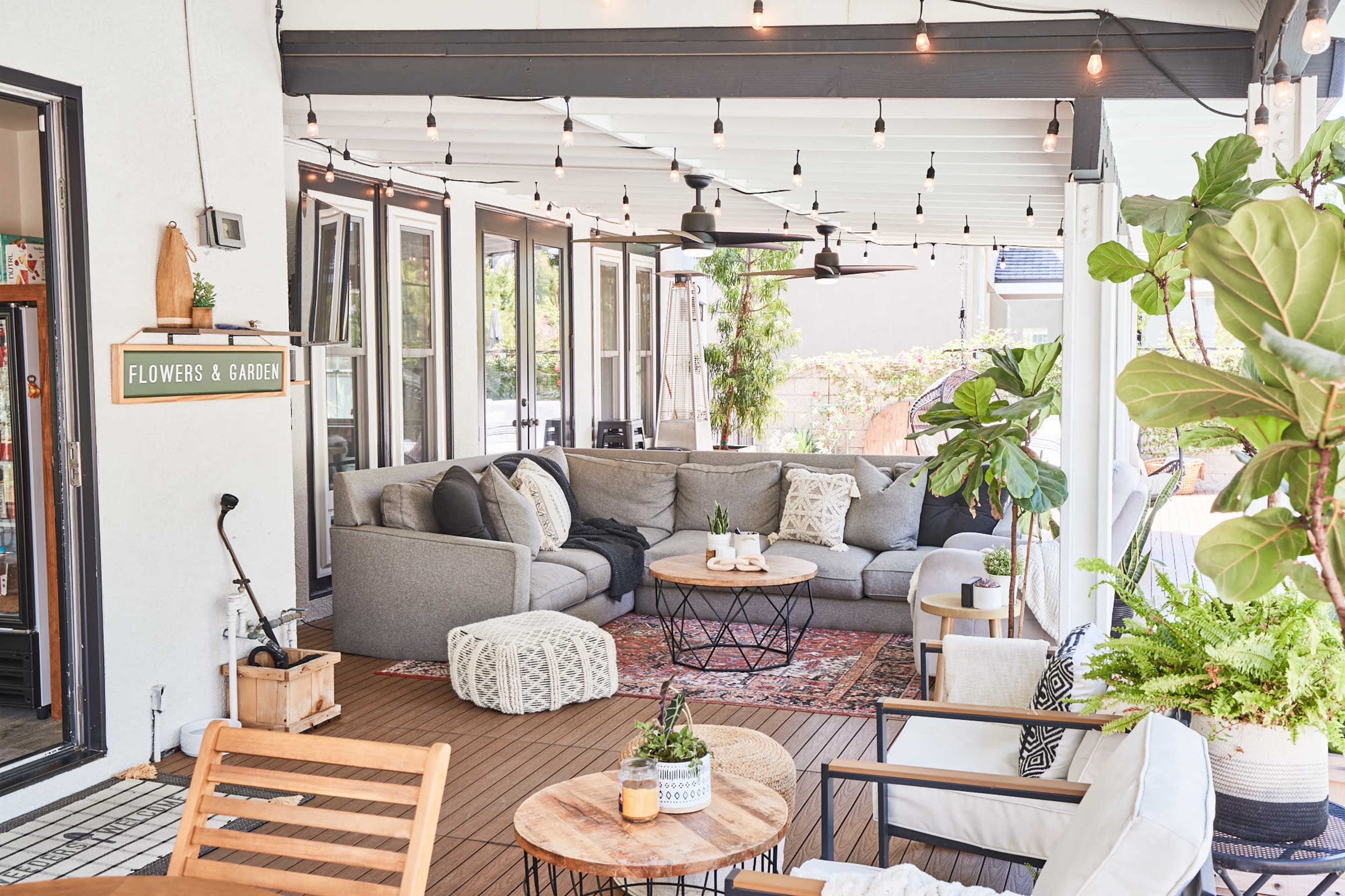 A spacious outdoor patio features a gray sectional sofa, a round coffee table, potted plants, and string lights overhead.