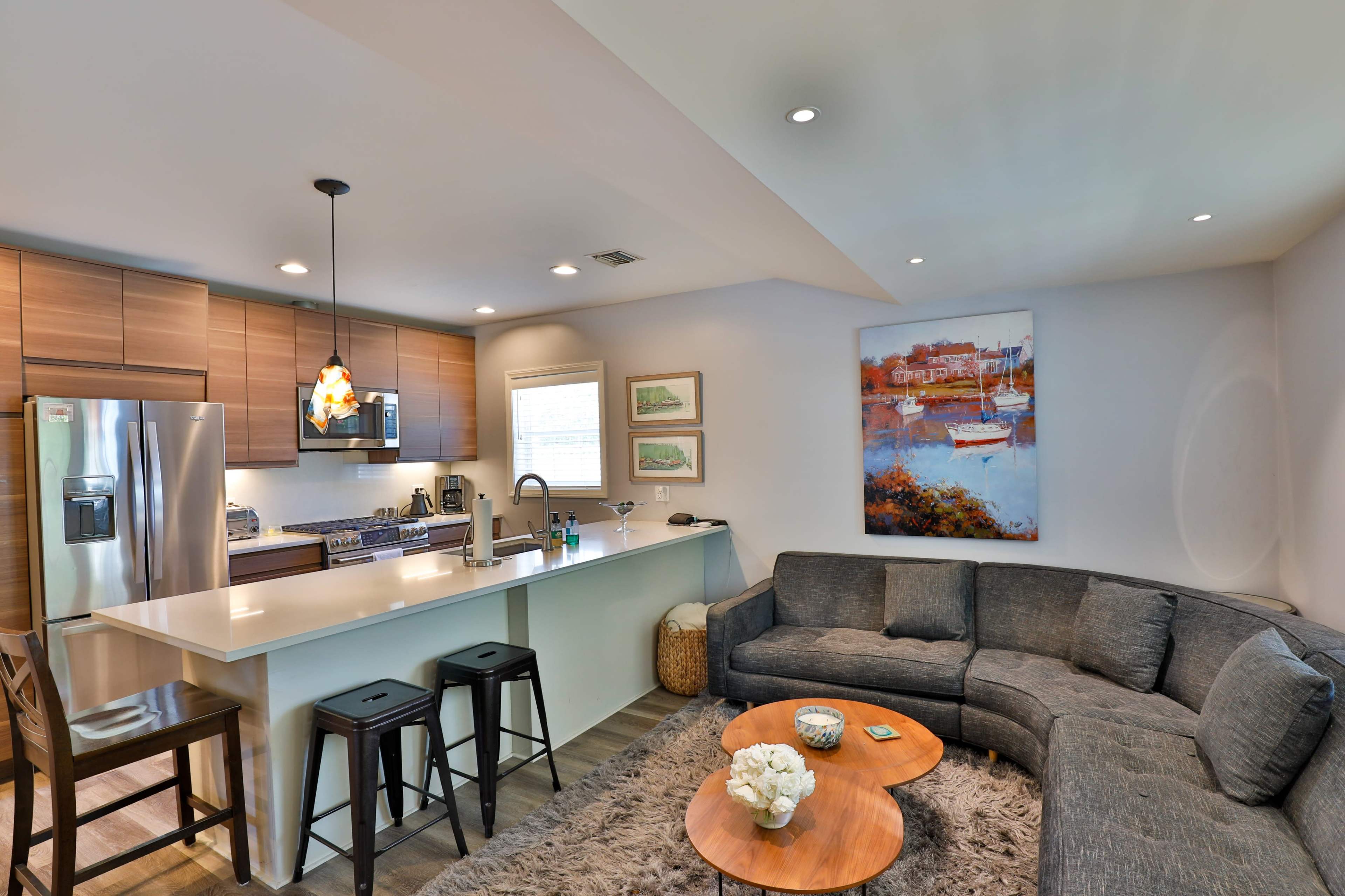 A modern living space features a sectional sofa, a wooden coffee table, and a kitchen with stainless steel appliances and bar seating.