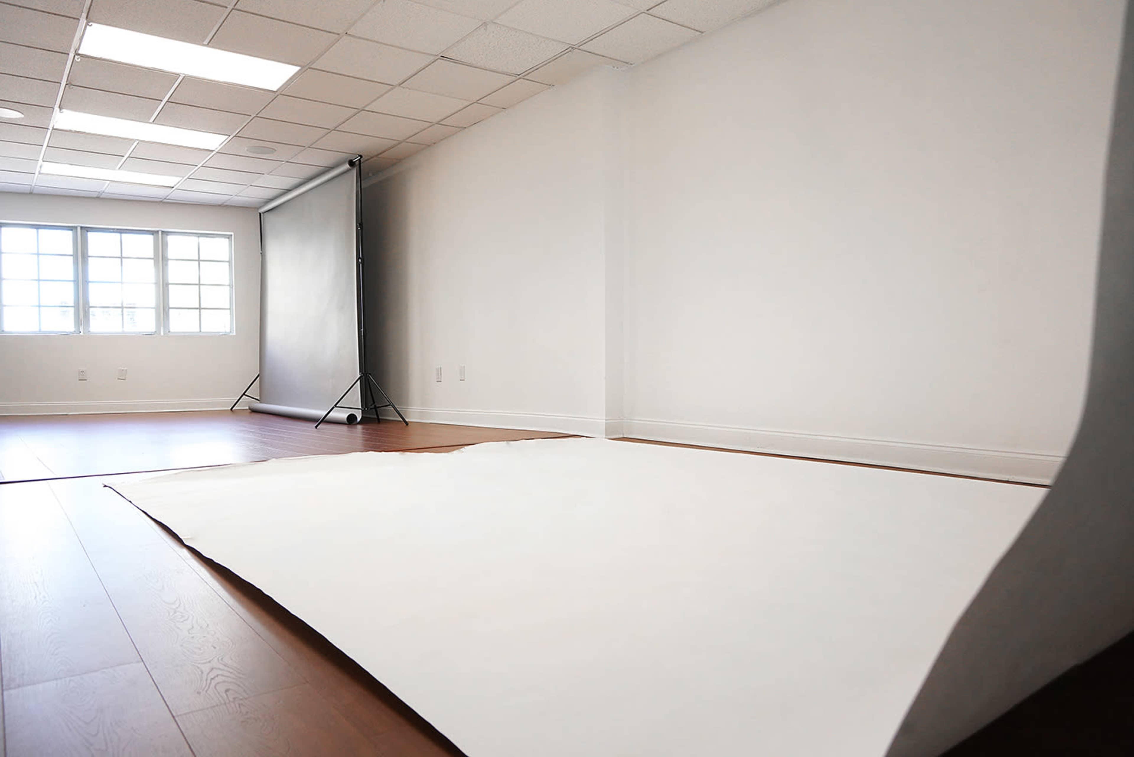 A minimalistic photography studio features a smooth white backdrop and wooden floors, with a large window providing natural light.
