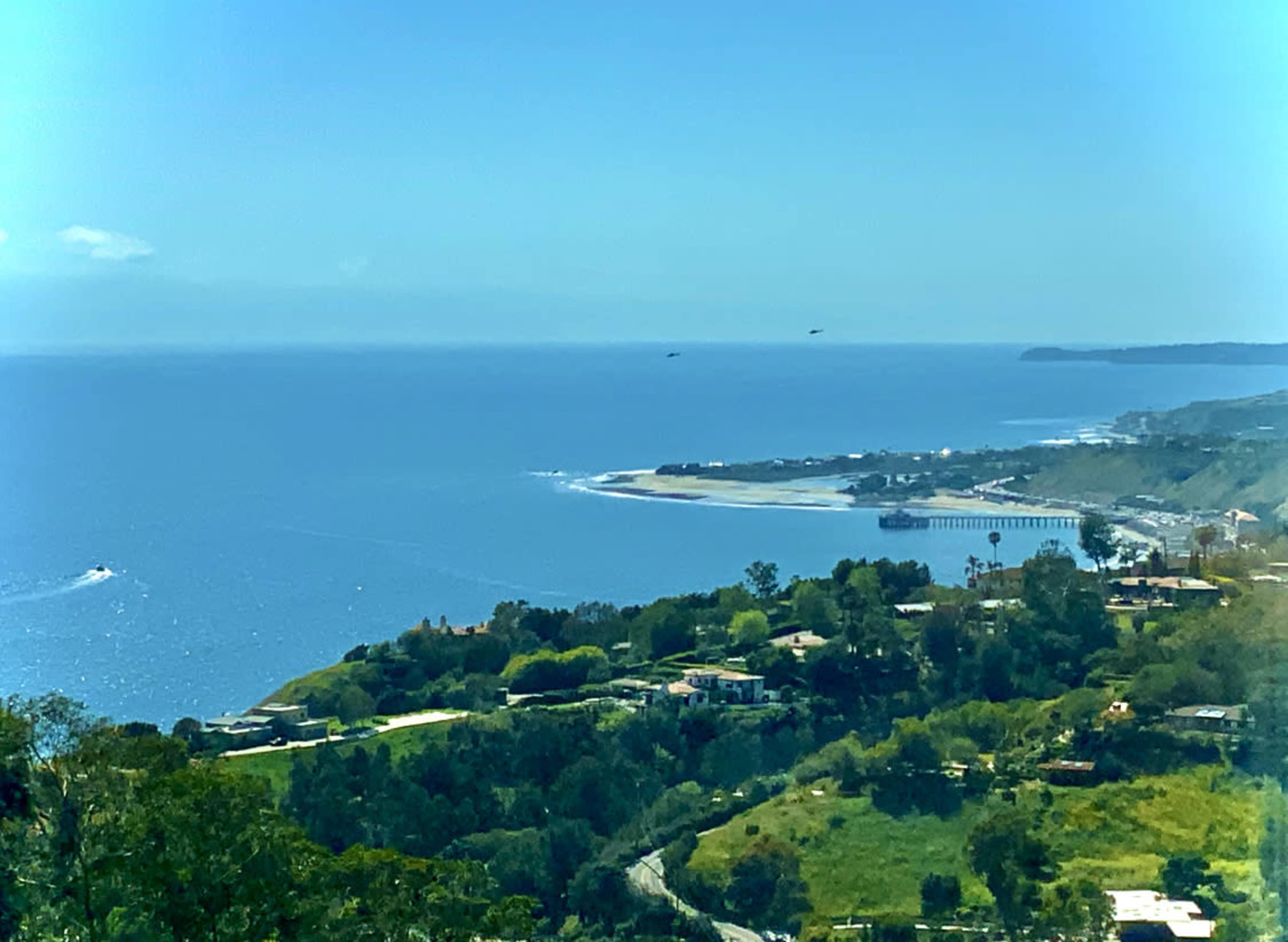 A coastal view featuring a sandy beach, a pier, and lush greenery in the foreground.
