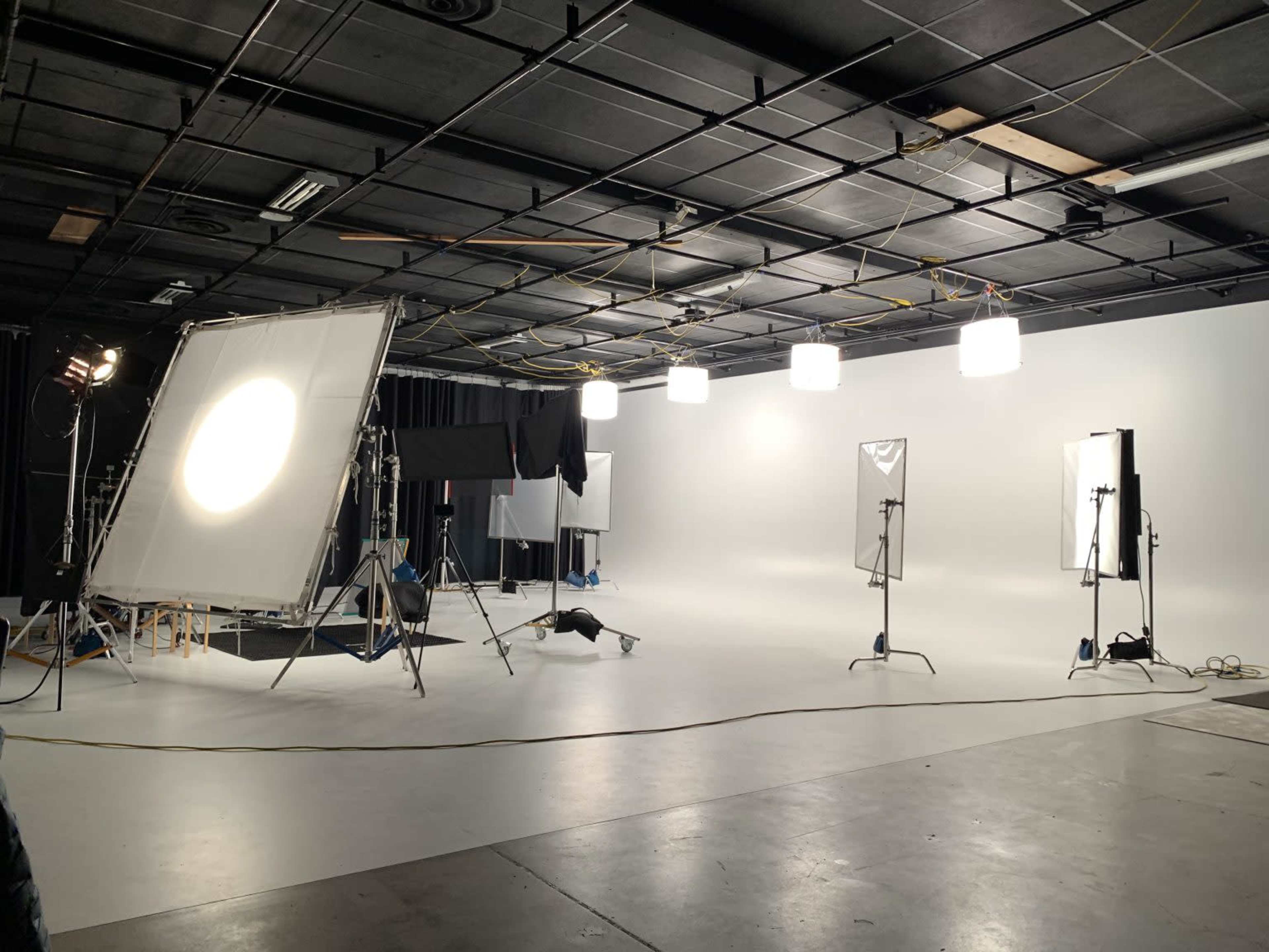 A photography studio with several lighting setups and a blank backdrop.