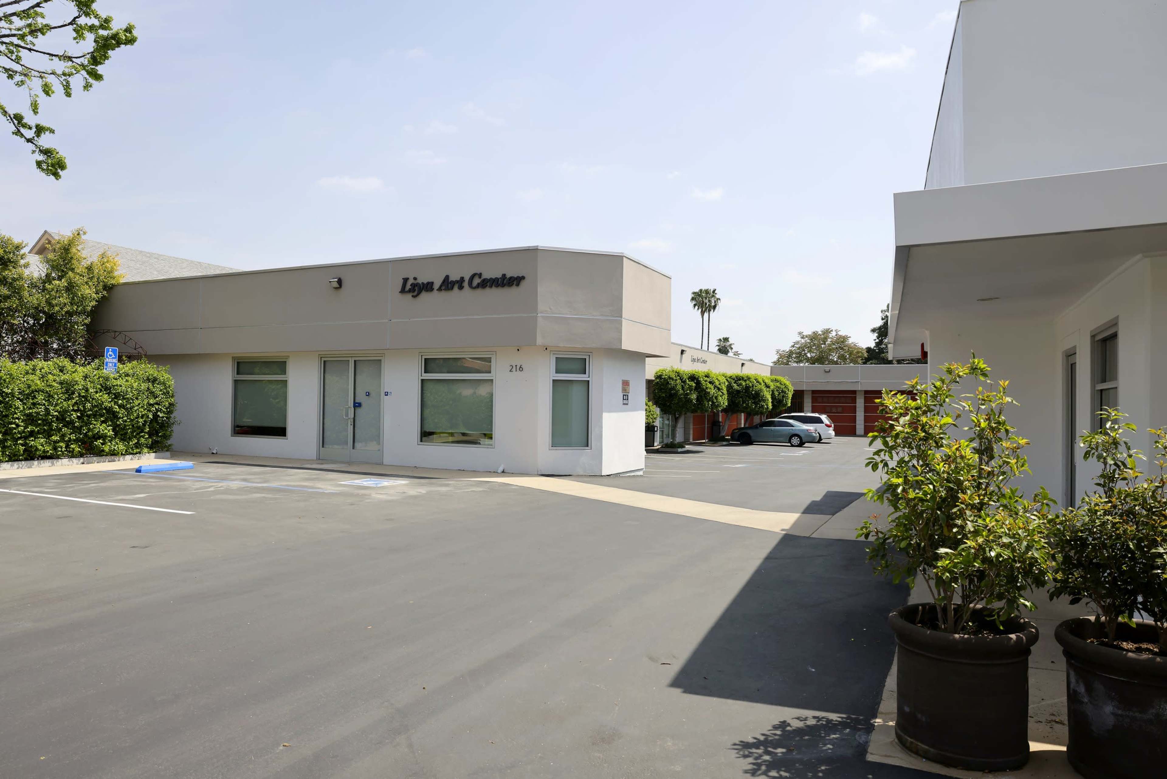 The exterior of the Lyna Art Center with a parking lot and adjacent buildings under a blue sky.