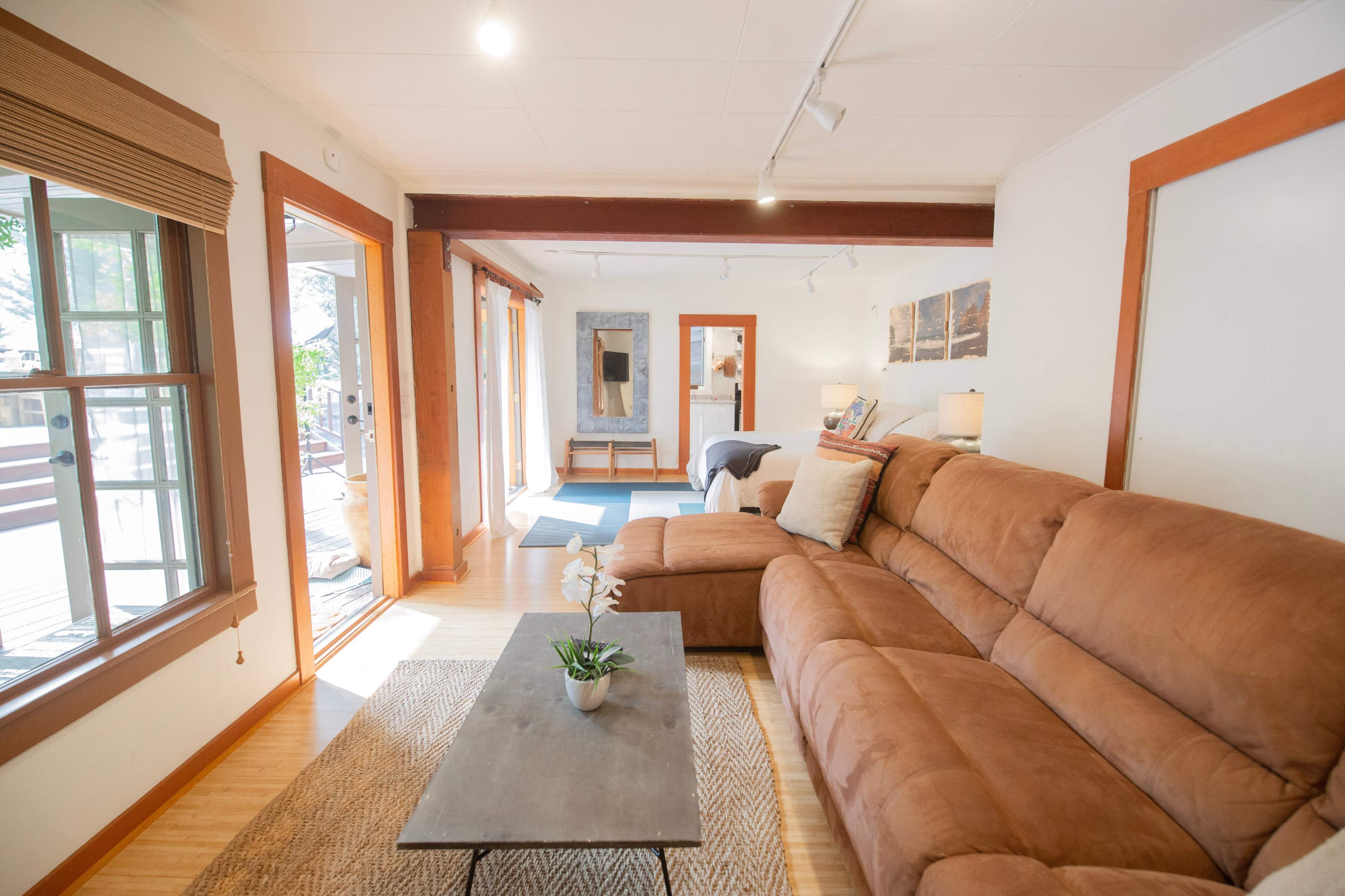 A bright living room with a brown sectional couch, a coffee table, and large windows that open to an outdoor space.