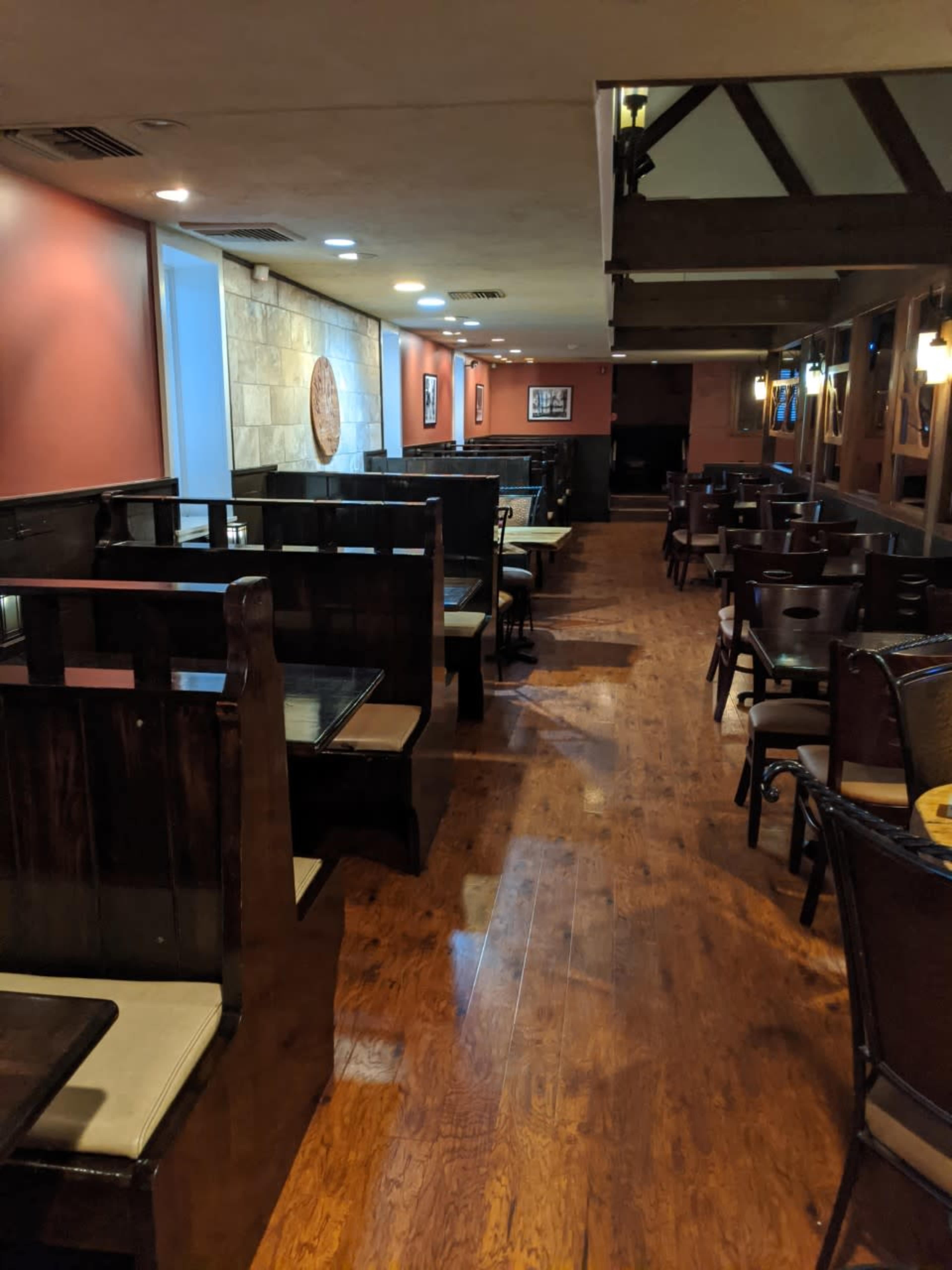 A restaurant interior featuring wooden booths along the walls and empty tables arranged throughout the space.