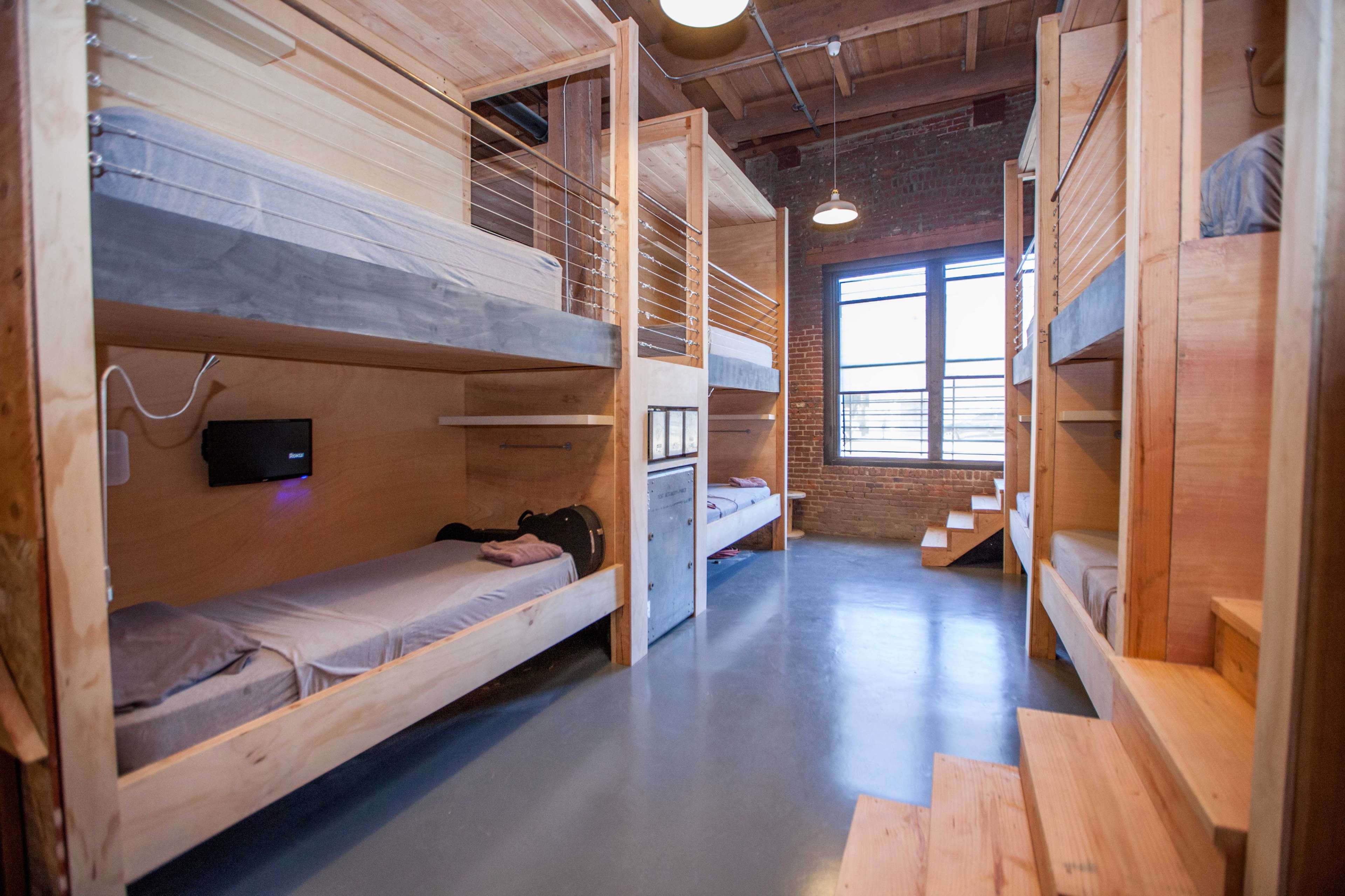 A modern bunk room with wooden bunk beds and a large window allowing natural light to enter.