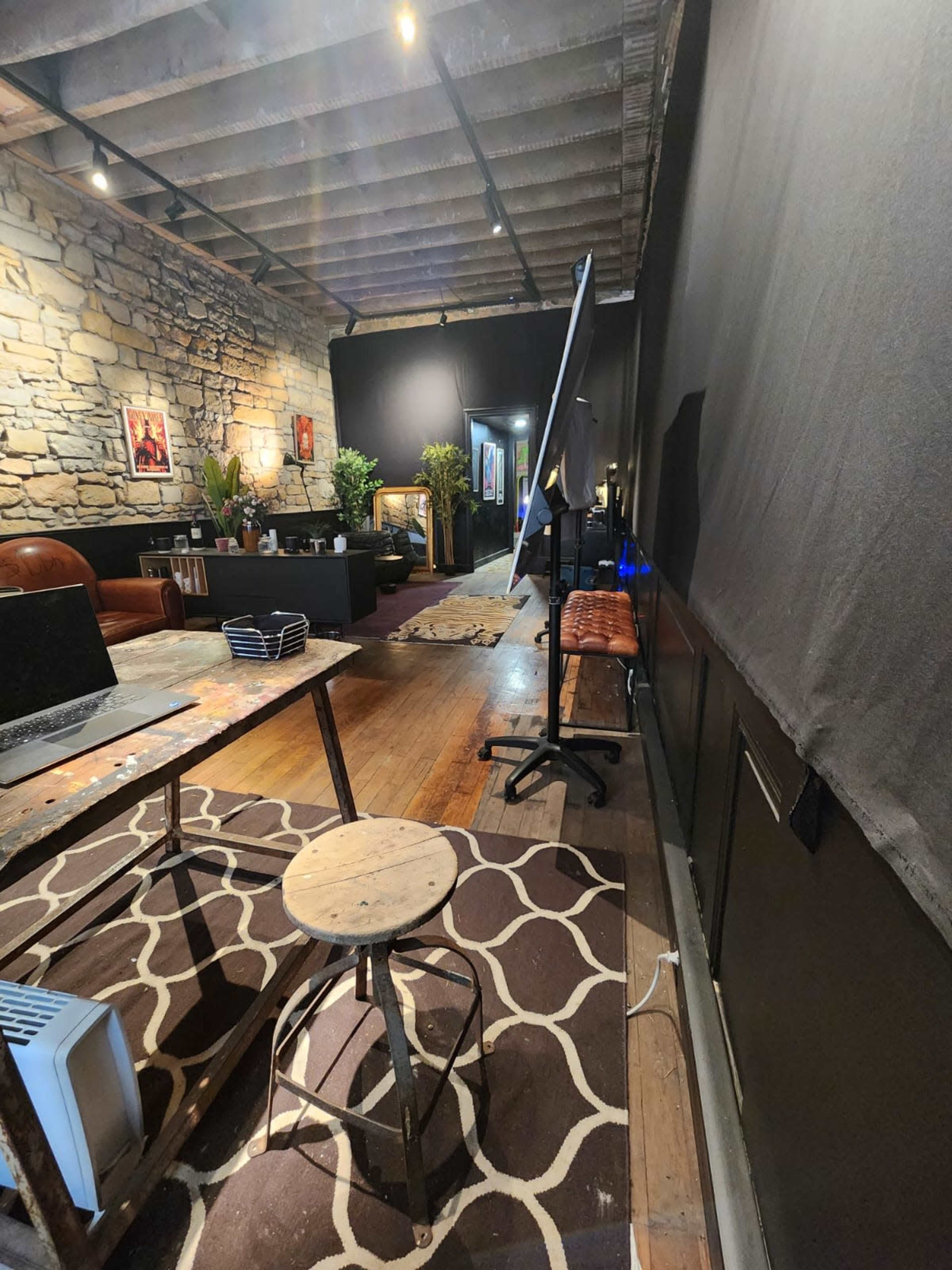 A spacious room with a stone wall, wooden beams, and various furniture pieces, including a table, chairs, and plants, arranged in a workspace setting.