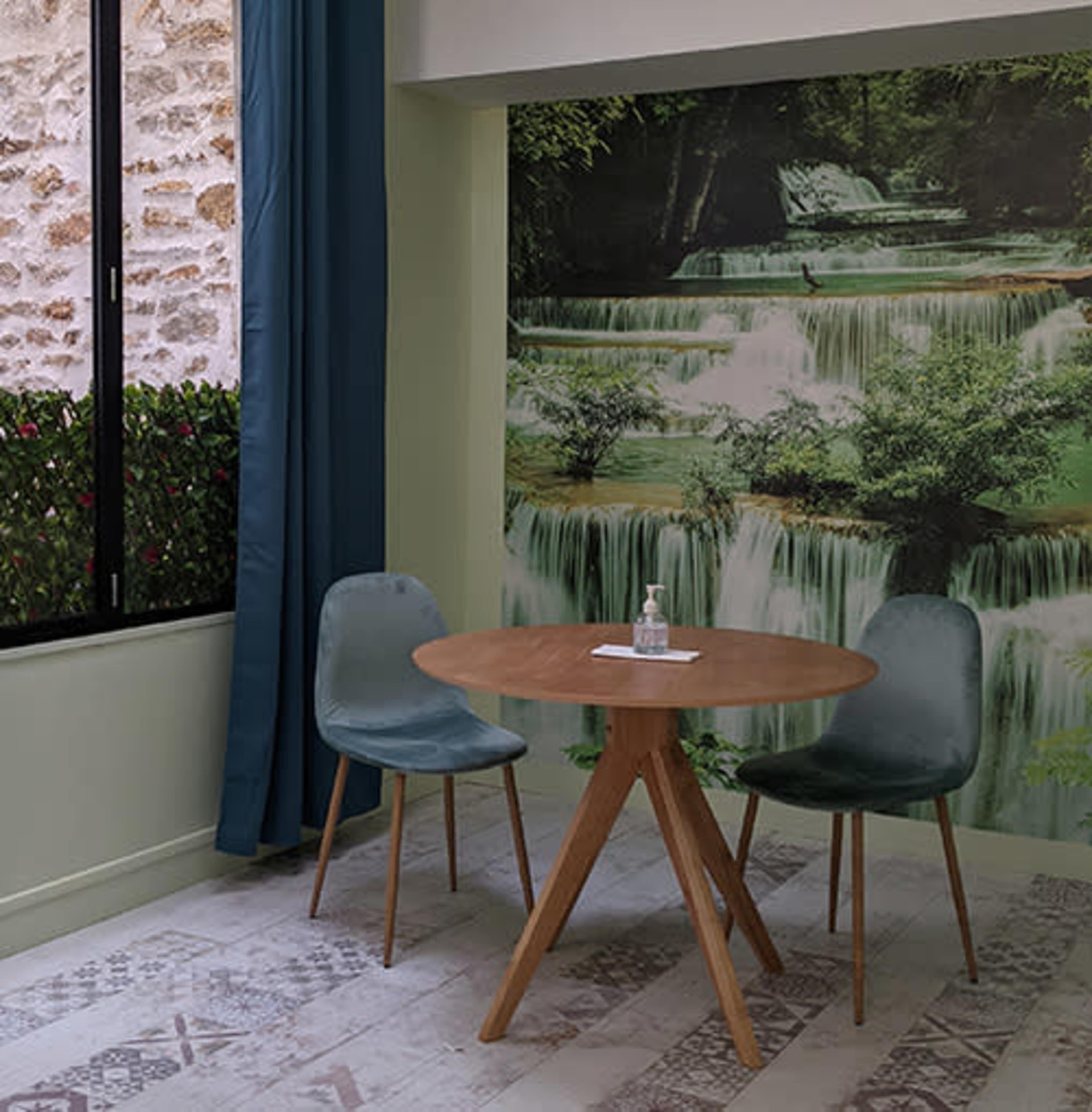A small dining area with a wooden round table and two green chairs in front of a mural of waterfalls.