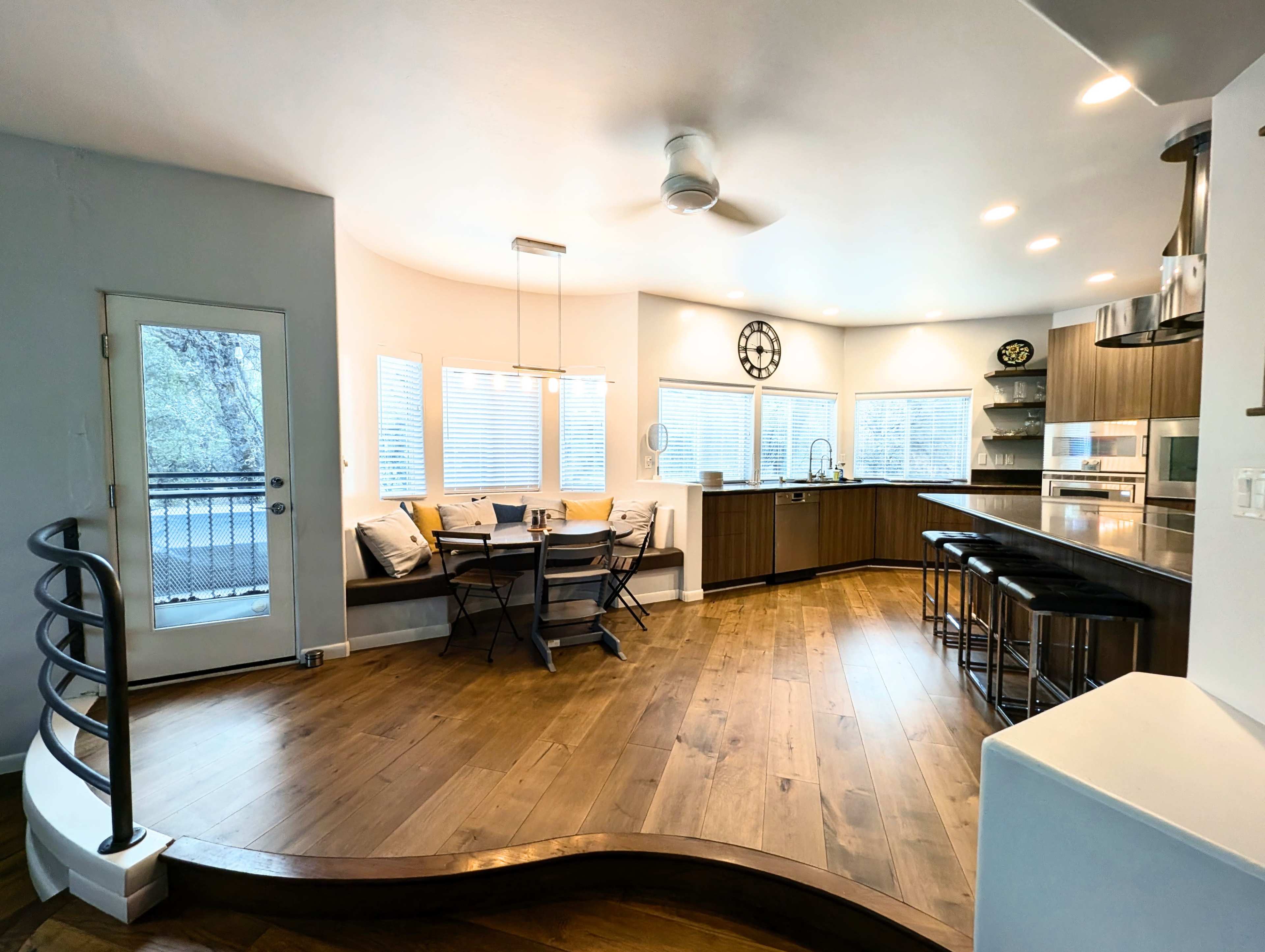 The image shows a modern kitchen with a circular dining area, large windows, and sleek wooden cabinetry.