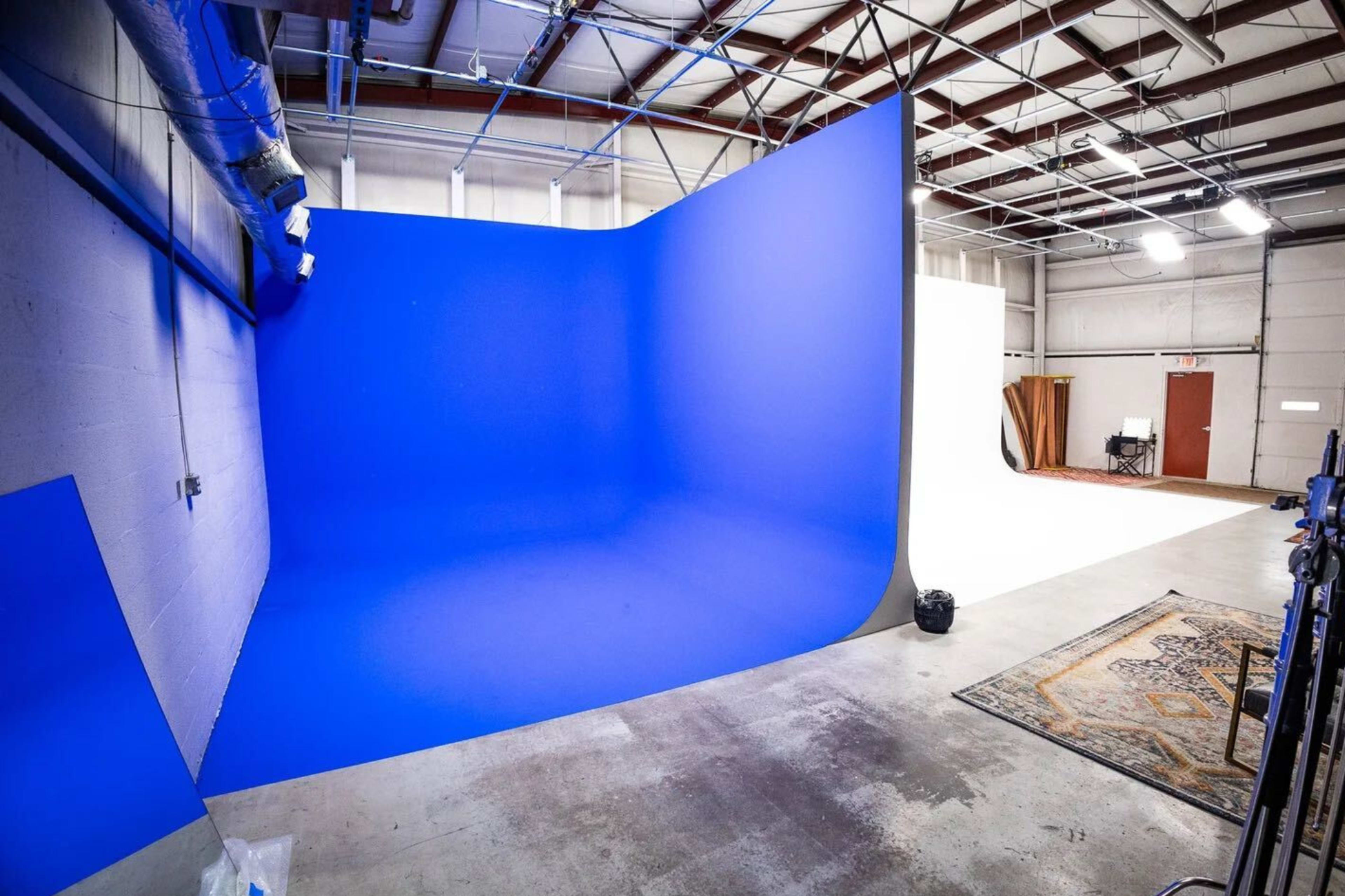 The image shows a spacious studio with a blue and a white backdrop set up against the walls, with various studio equipment and a rug on the floor.