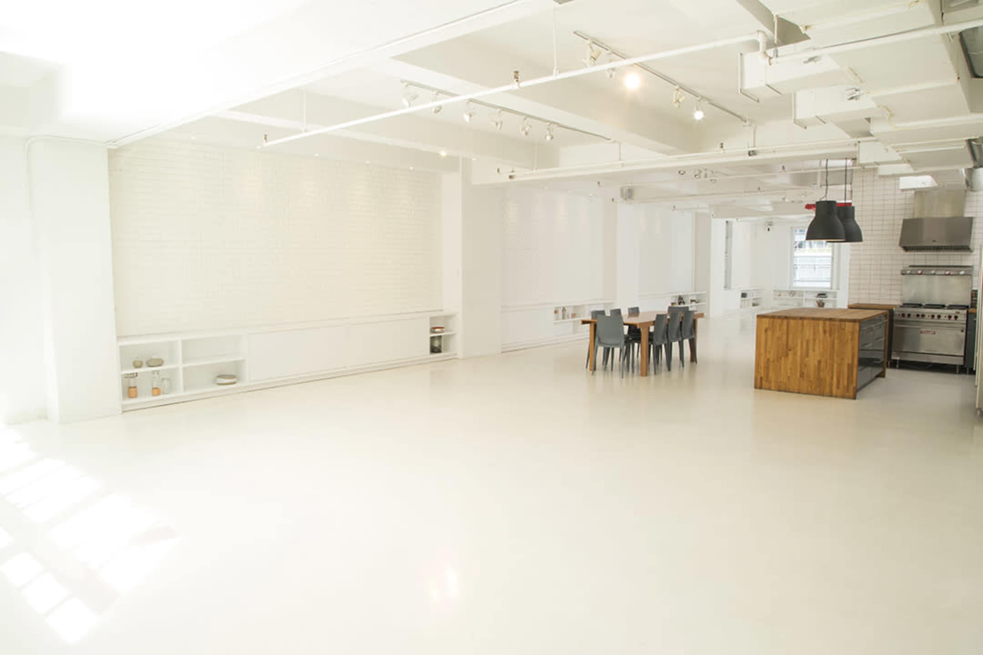 A bright, spacious kitchen with a long wooden dining table, metal chairs, and industrial kitchen appliances.