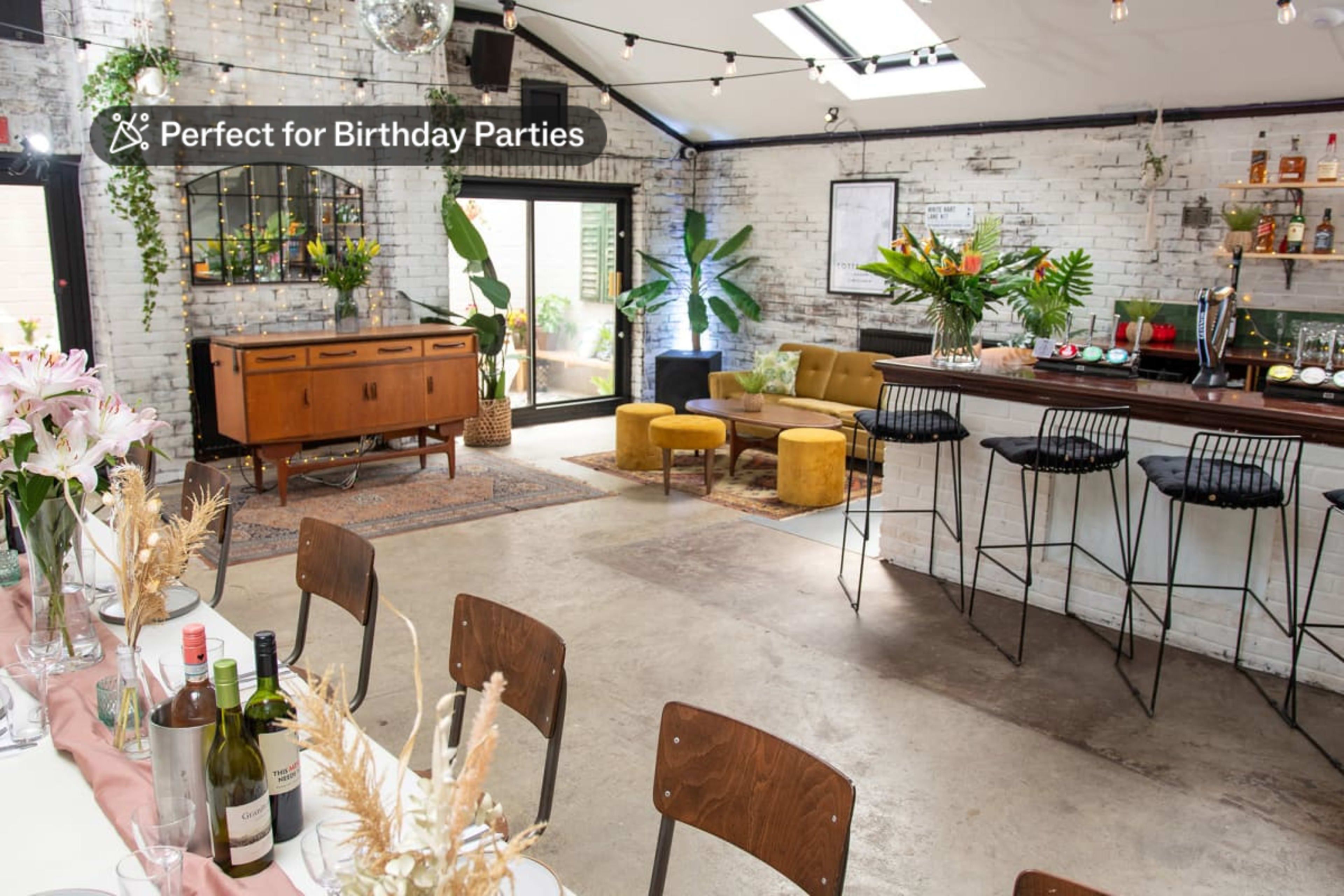 A spacious, decorated interior with a bar, seating area, and a long dining table set for an event.