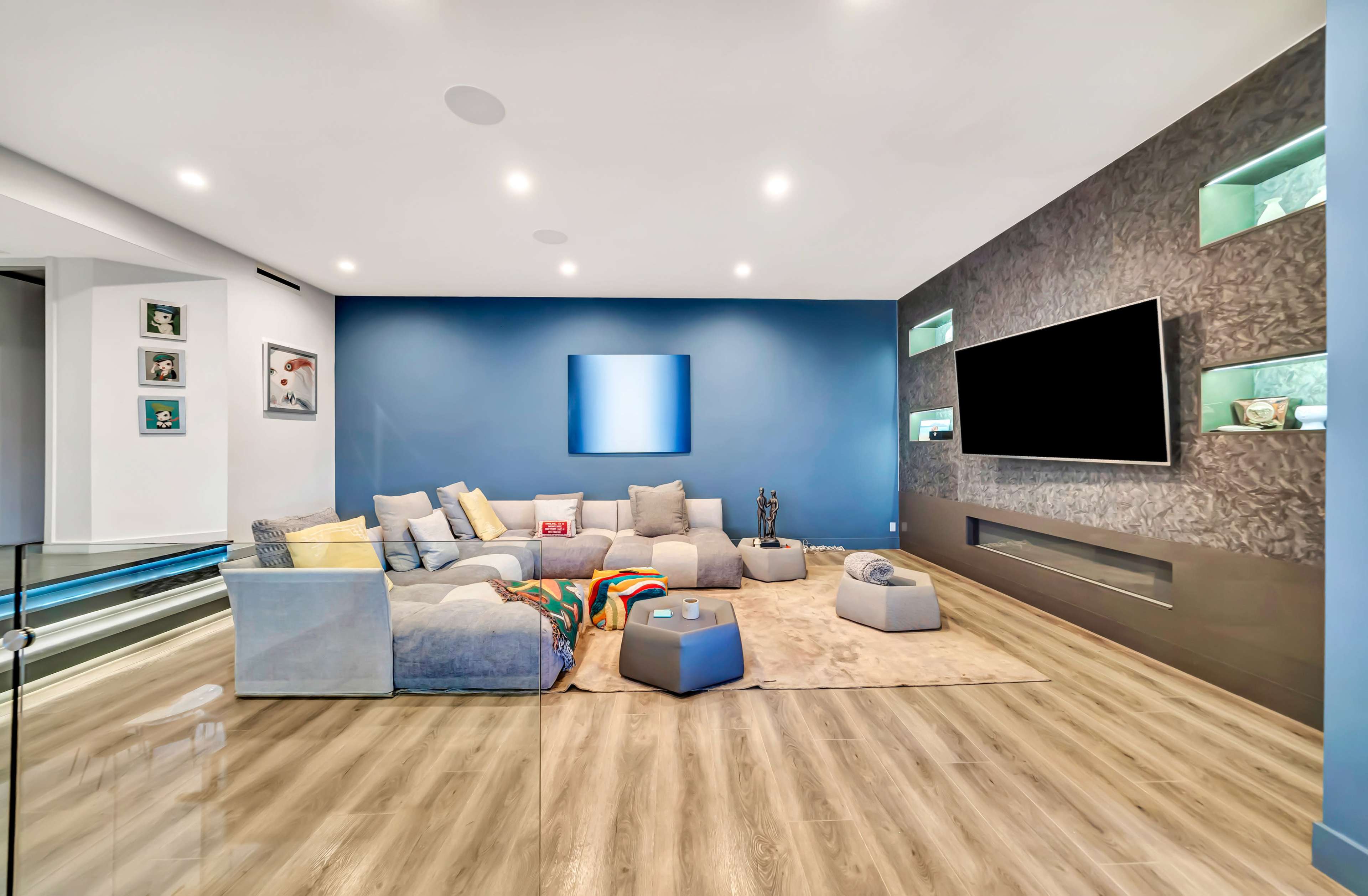 A modern living room with a large sectional sofa, a flat-screen TV mounted on a wall, and decorative shelves.