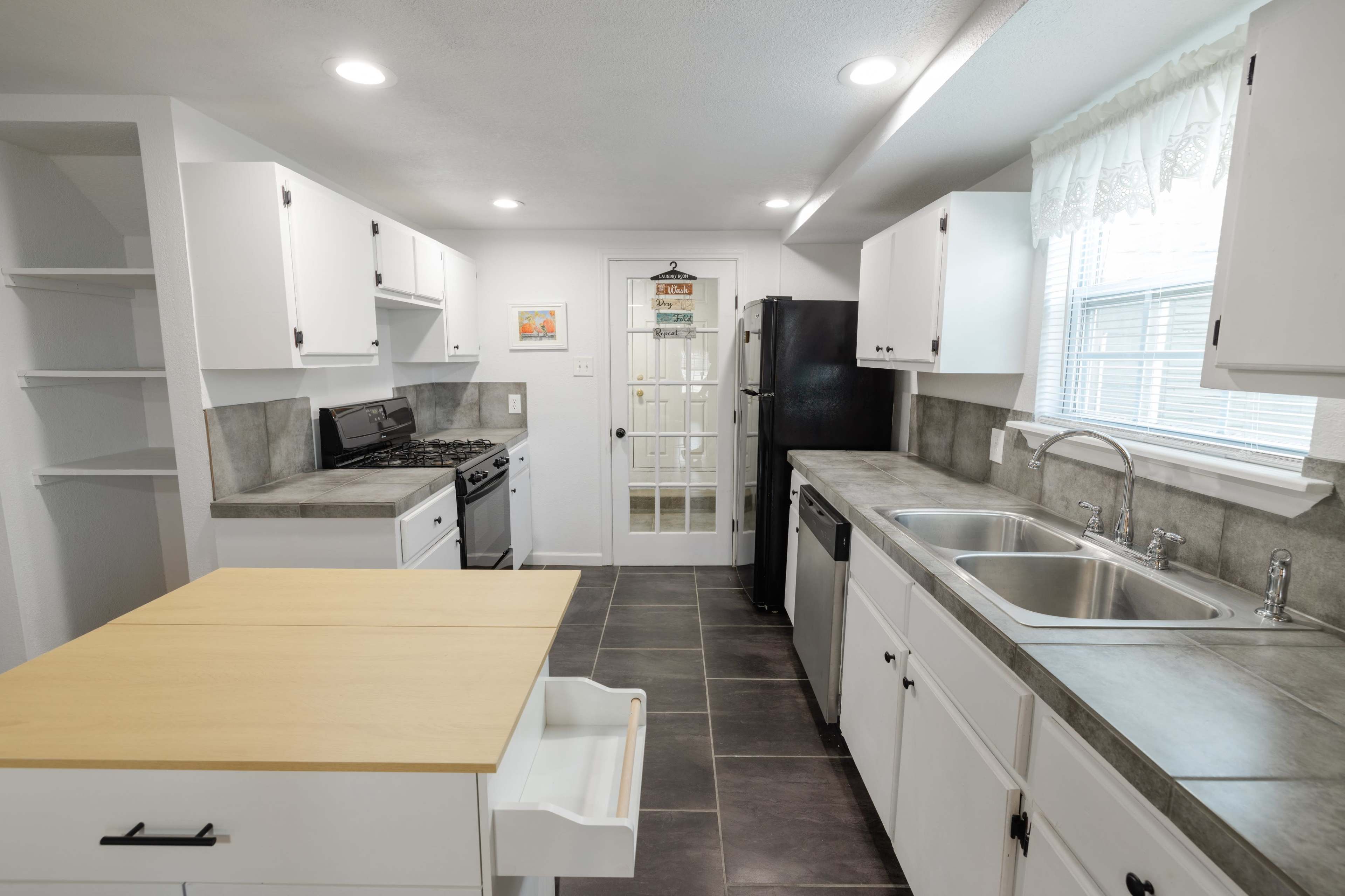 The image shows a modern kitchen with white cabinets, gray countertops, and stainless steel appliances, including a gas stove and a dishwasher.