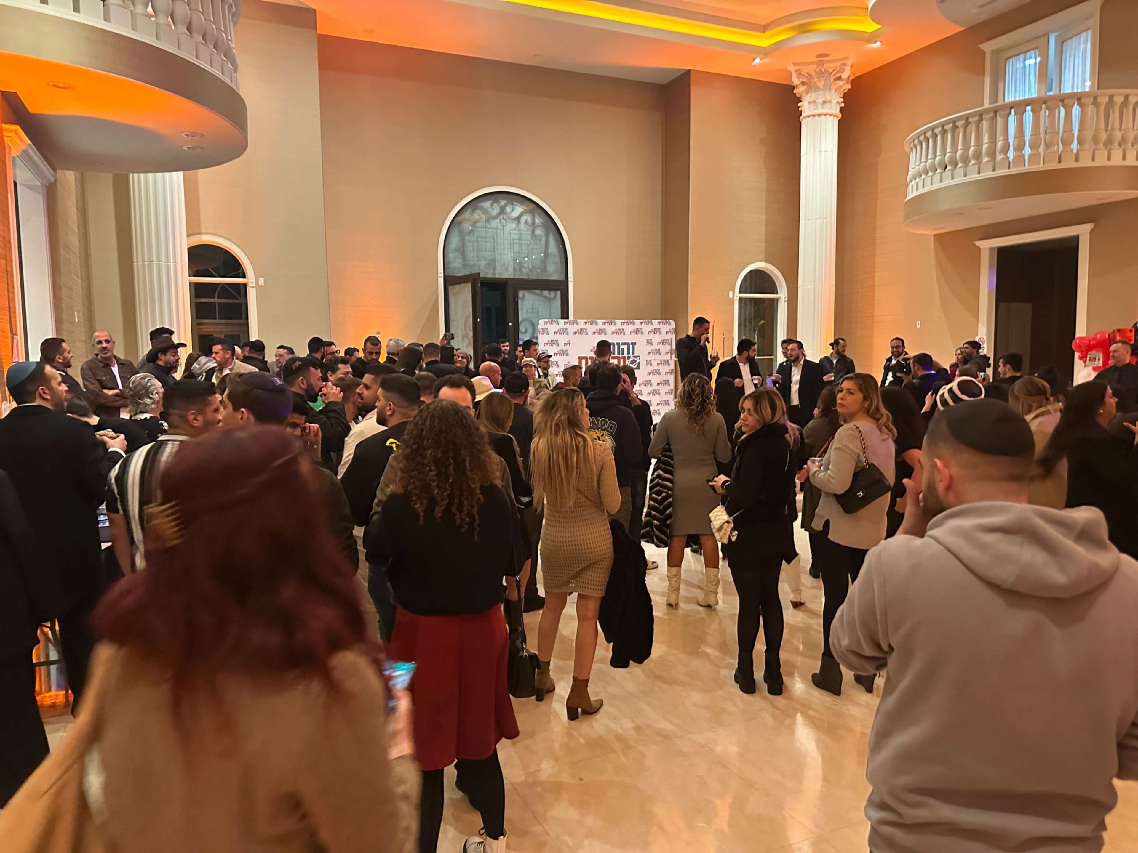 A large crowd gathers in a lavish indoor space, engaged in conversation and networking at an event.