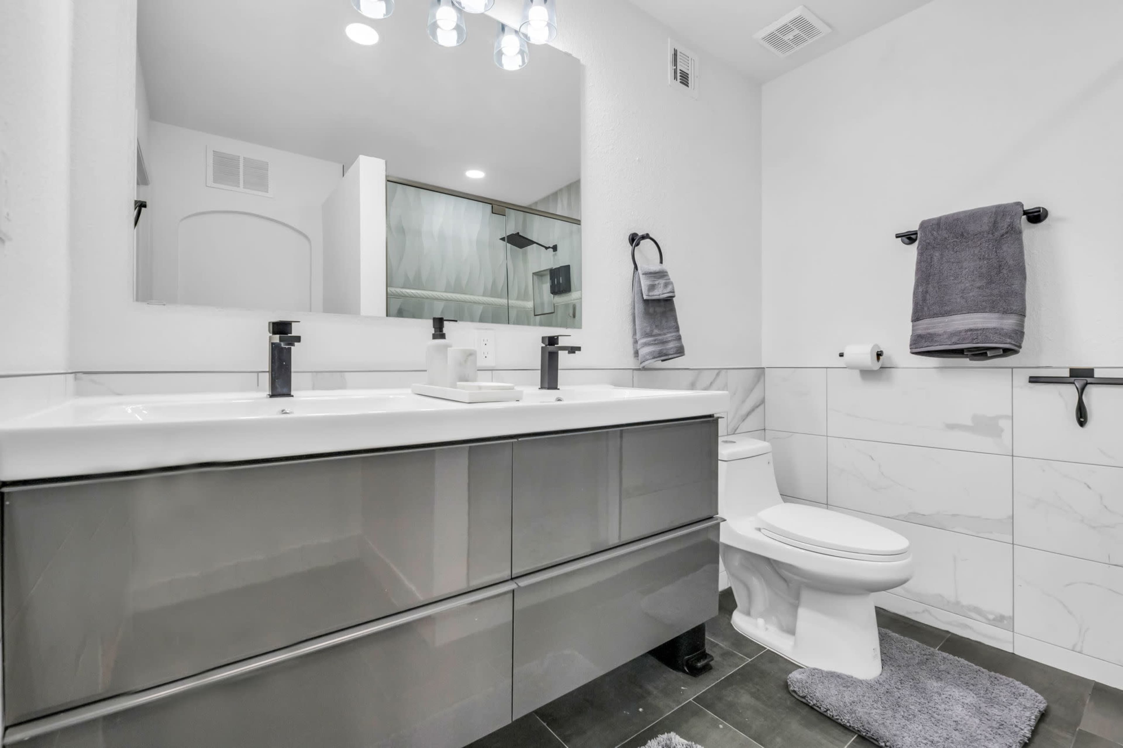 A modern bathroom featuring a sleek vanity with a sink, a toilet, and gray and white tiled walls.