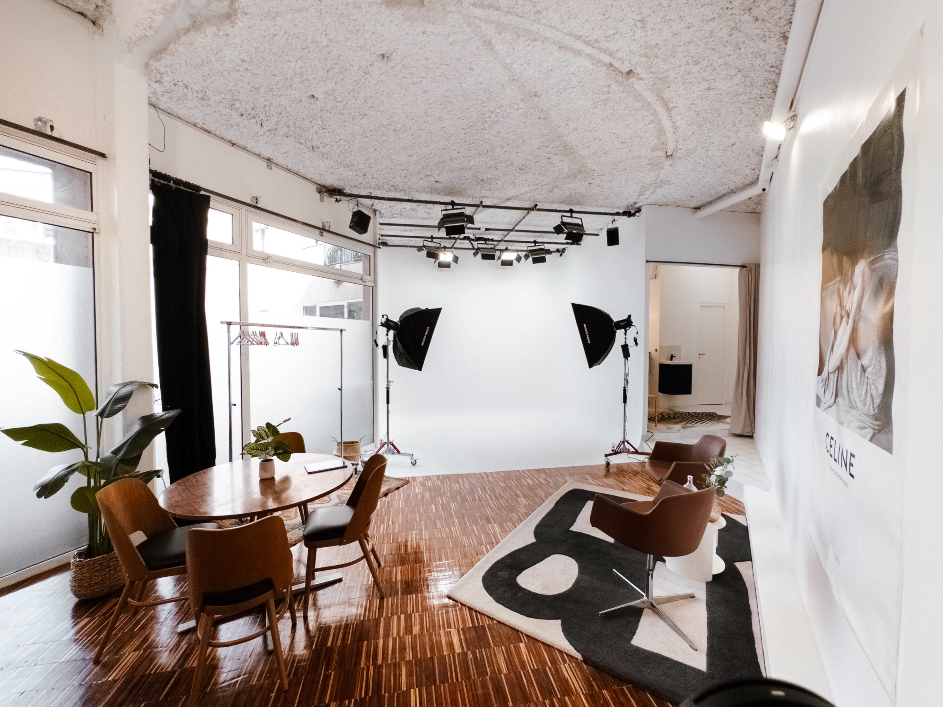The image shows a spacious studio with a circular dining table and chairs, a large white backdrop, and professional lighting equipment set up for photography.