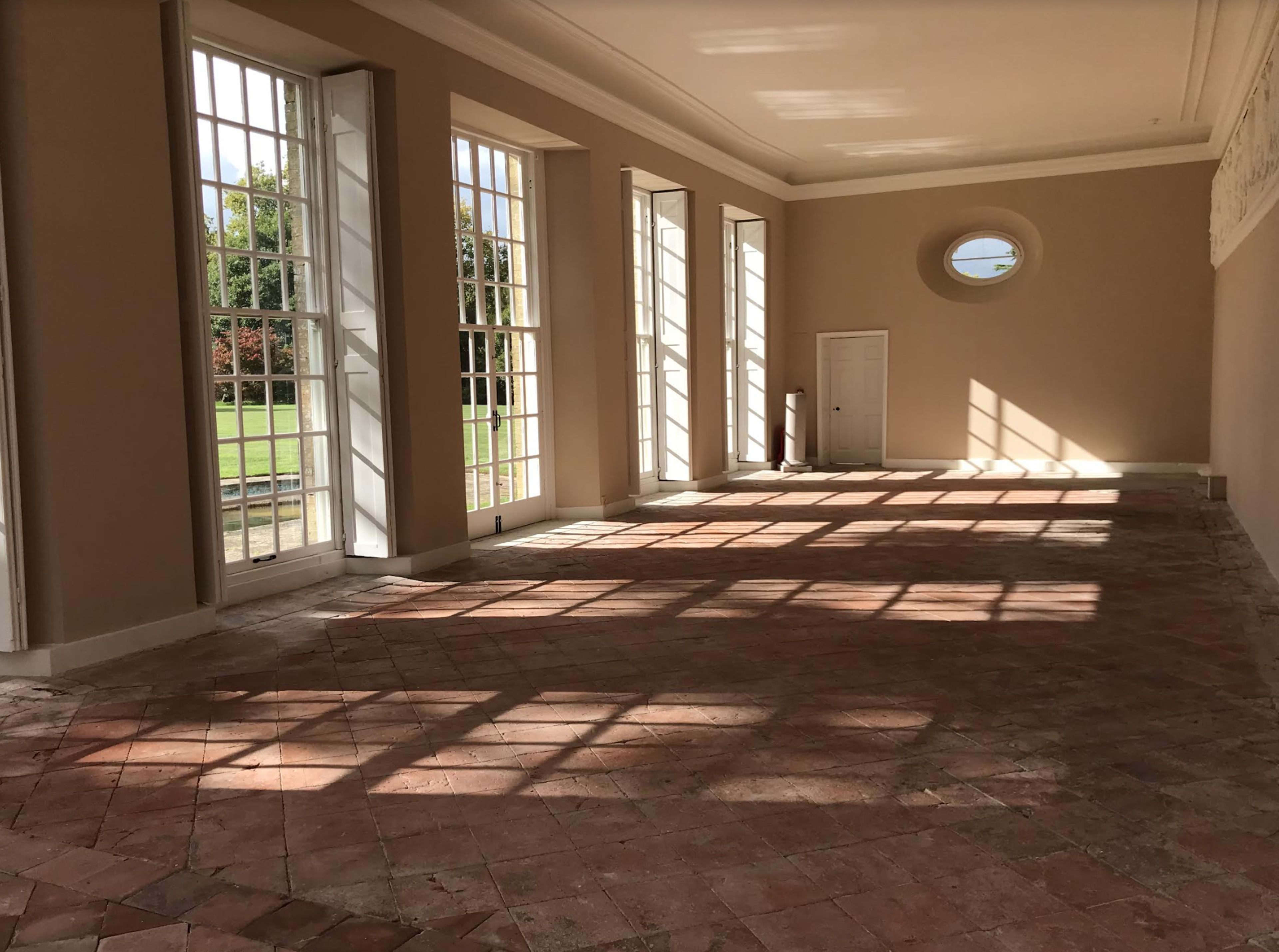 A spacious room with large windows allows sunlight to cast long shadows on the tiled floor.